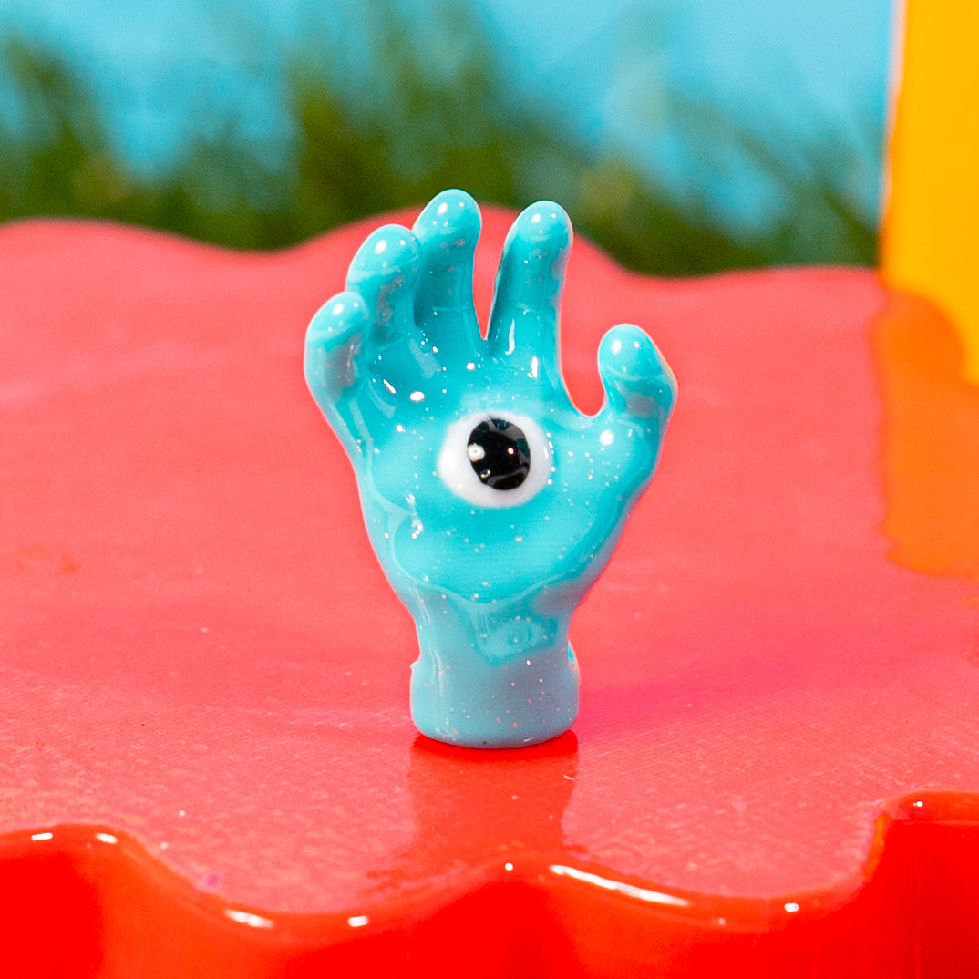 Close-up of a blue all seeing hand kandi bead with a single eye in the palm on a red riser