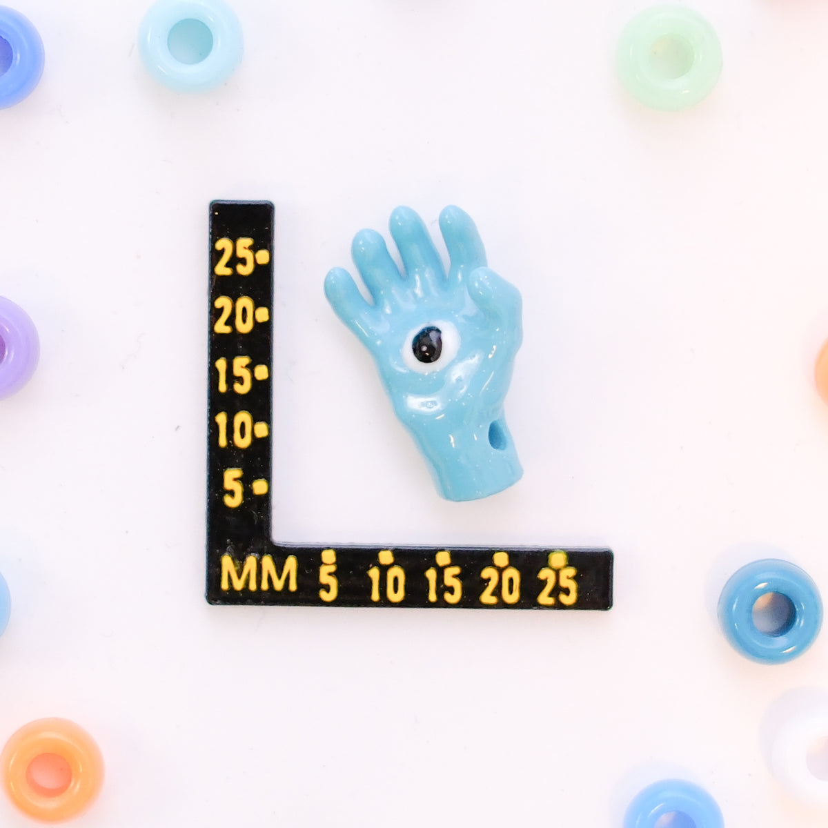 Size guide: an all seeing hand kandi bead beside a millimeter ruler for scale