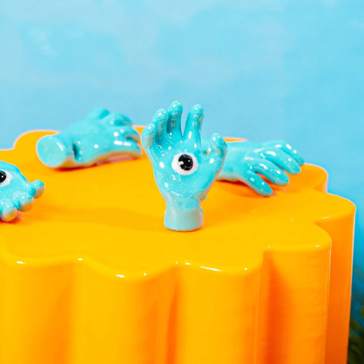 Upright all seeing hand kandi bead on an orange riser with more hands lying around it