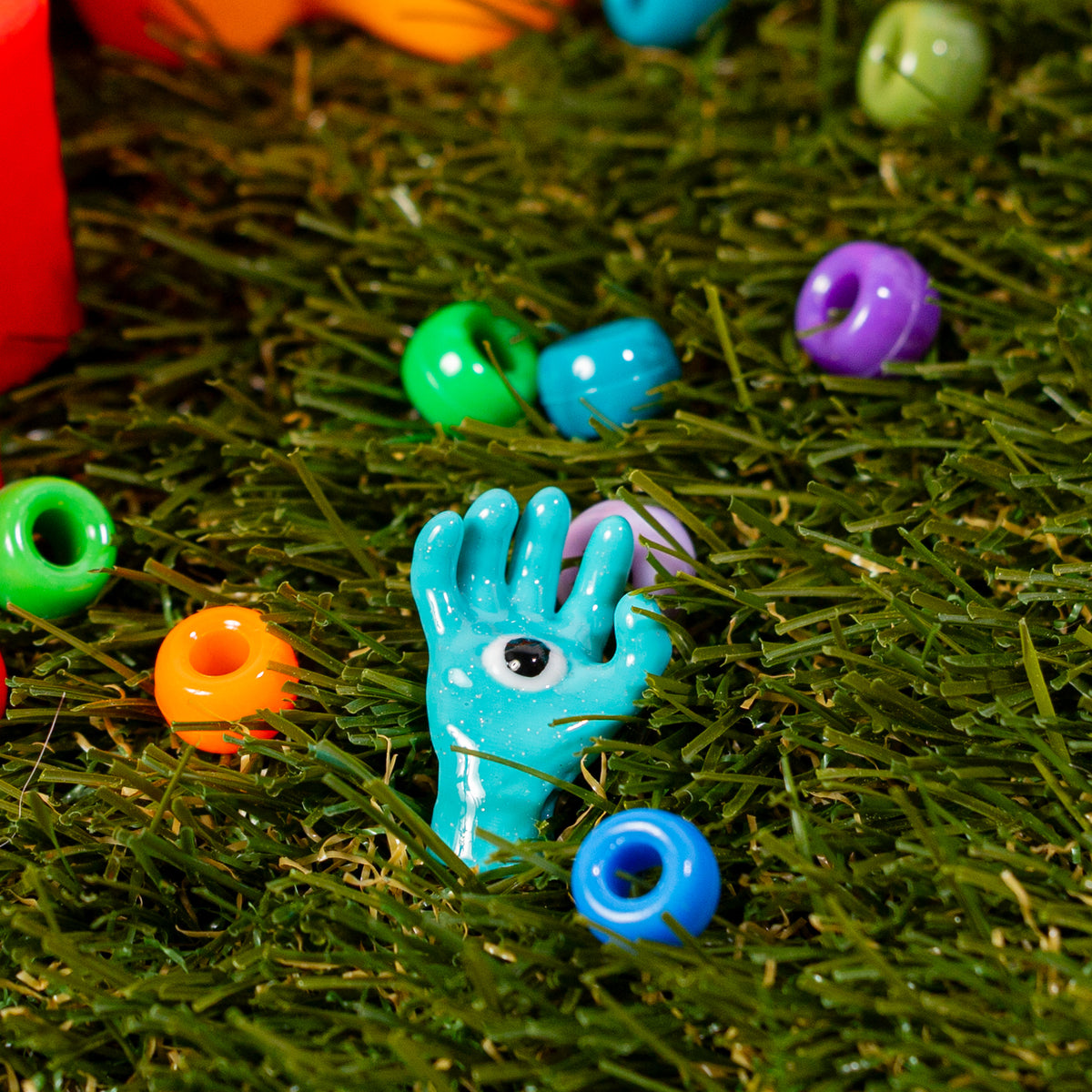 Blue all seeing hand kandi bead reaching out of green grass among colorful beads