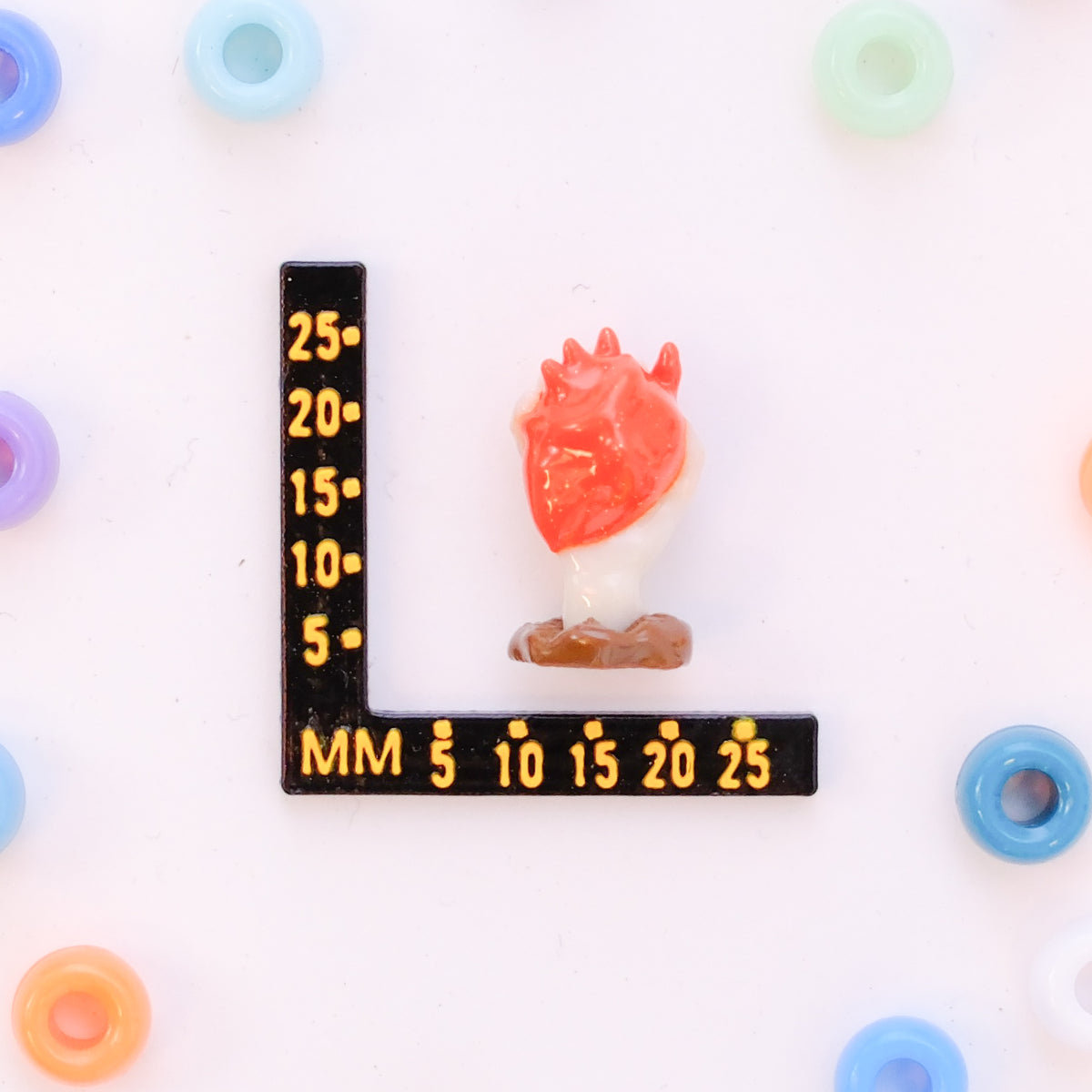 Size guide: an anatomical heart hand kandi bead beside a millimeter ruler for scale