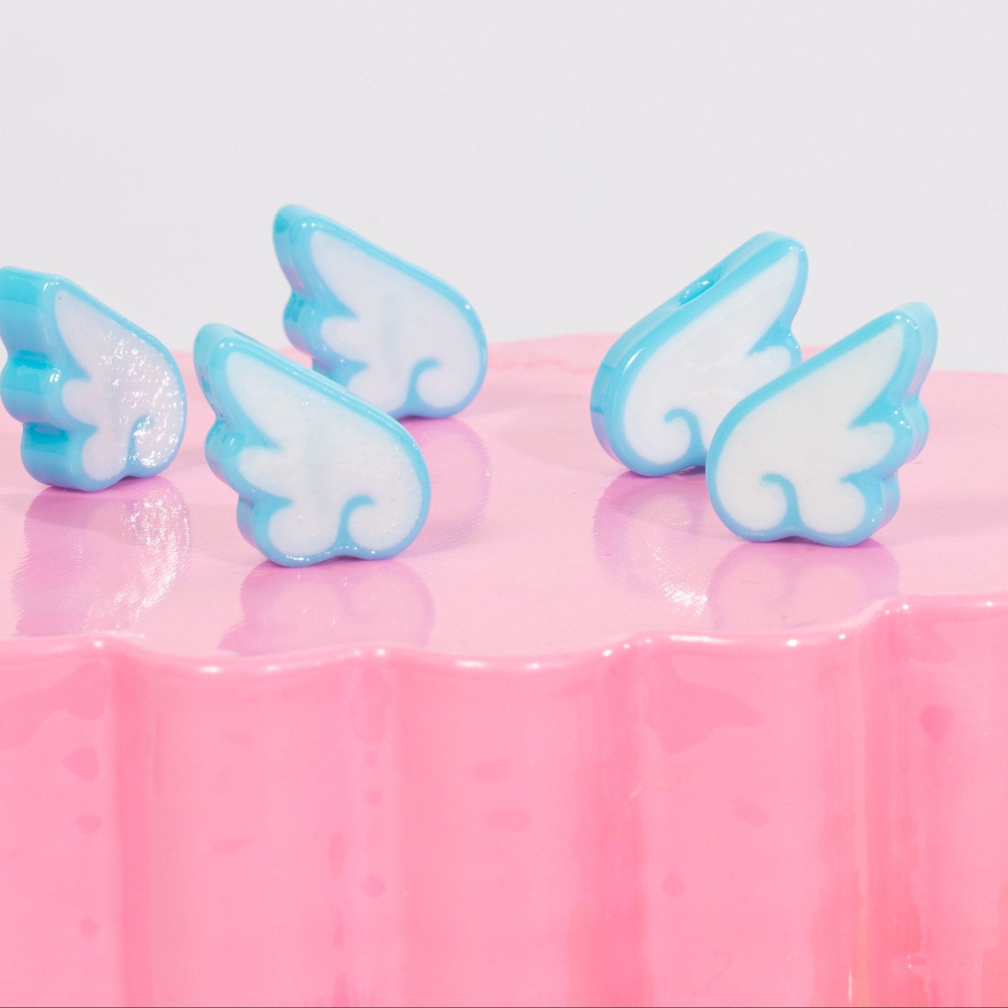 White-and-sky-blue angel wing kandi beads scattered on a glossy pink riser