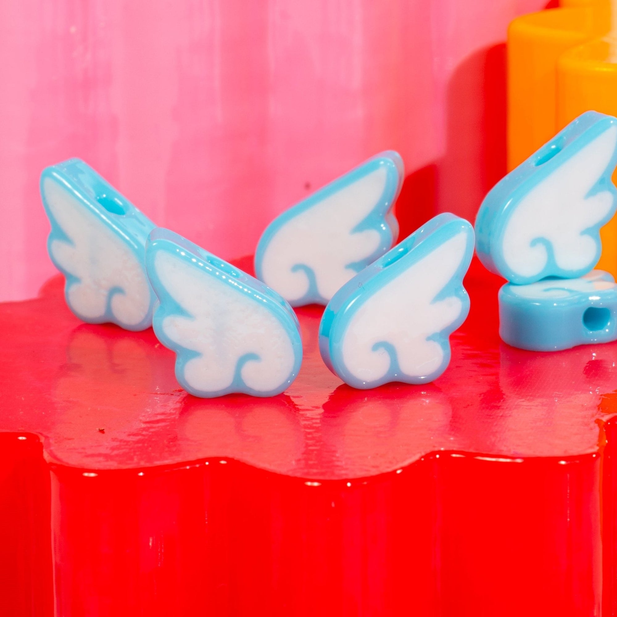 Close-up row of white-and-sky-blue angel wing kandi beads on a red riser, pink backdrop