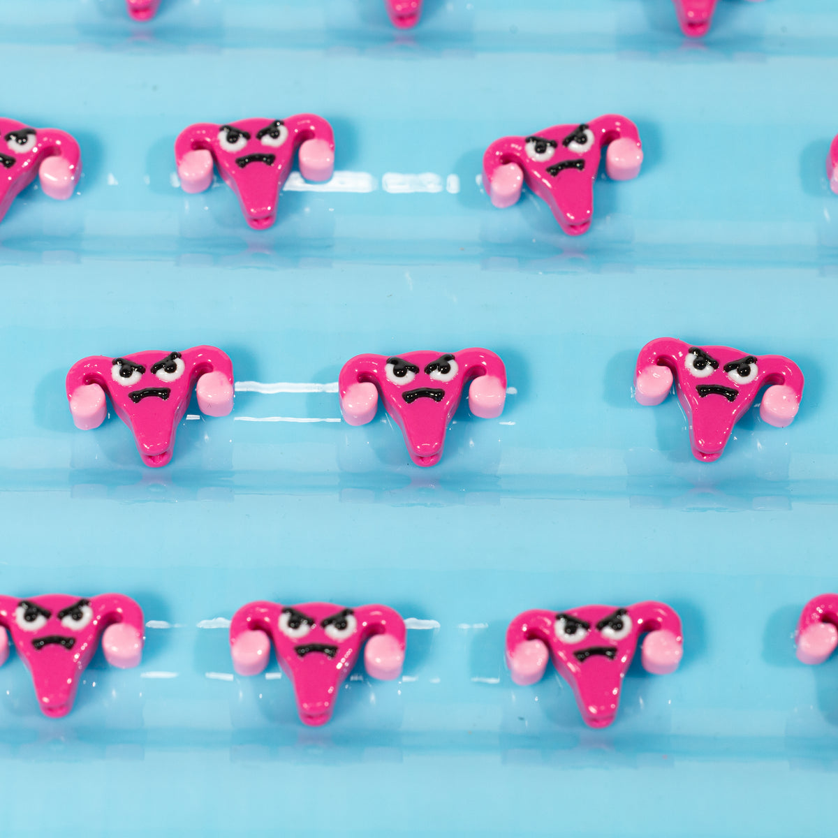 Rows of hot pink angry uterus kandi beads with frowning faces on pale blue