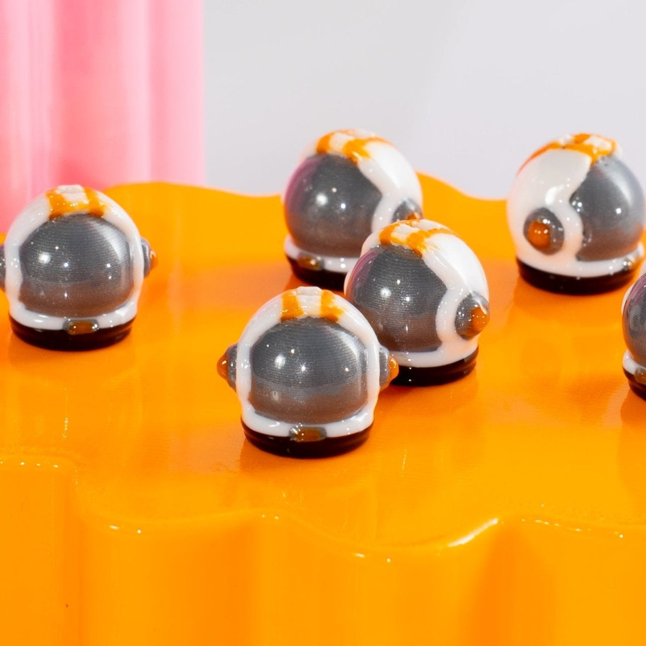 Silver and white astronaut helmet kandi beads clustered on a glossy orange riser at eye level