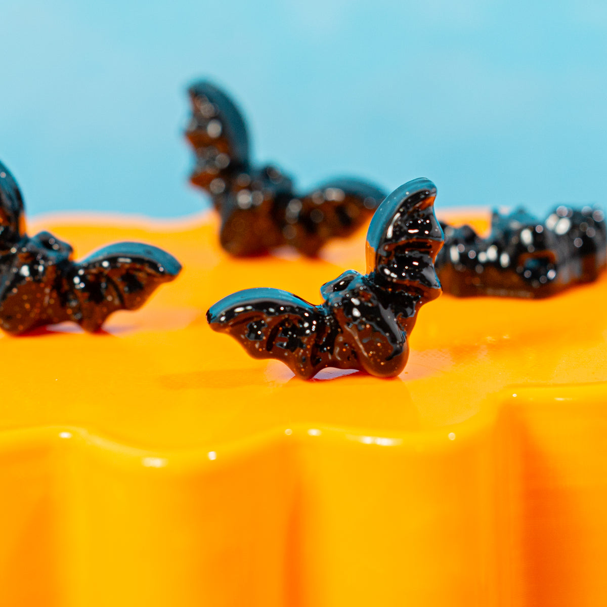 Close-up of glossy black bat kandi beads perched on an orange riser, blue behind