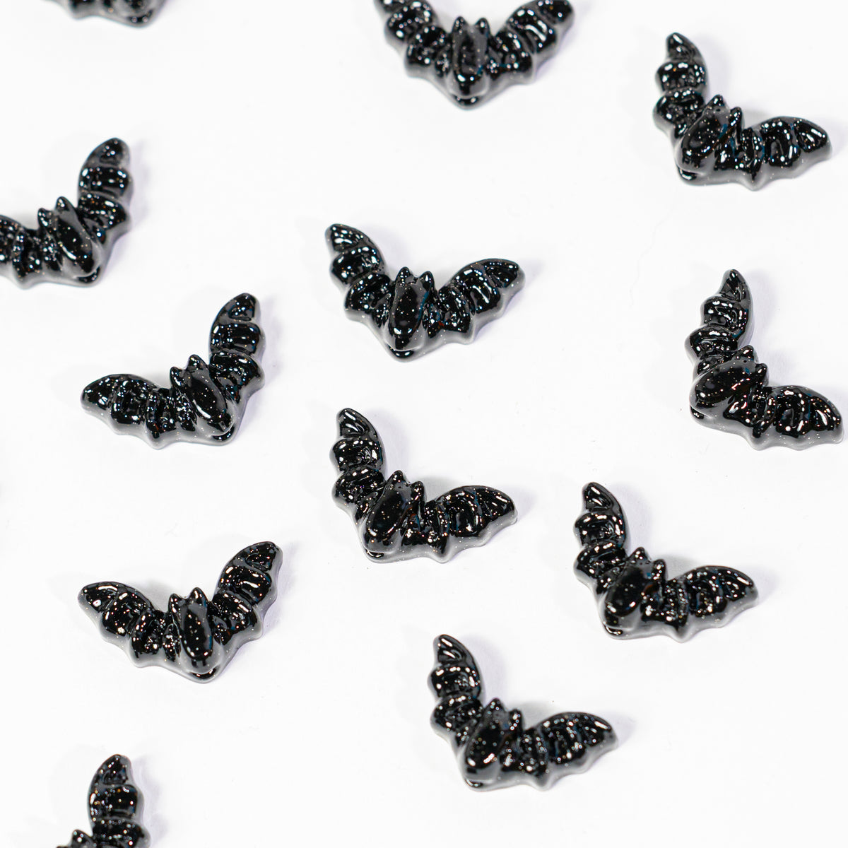 Black bat kandi beads with spread wings scattered on white, drilled holes visible