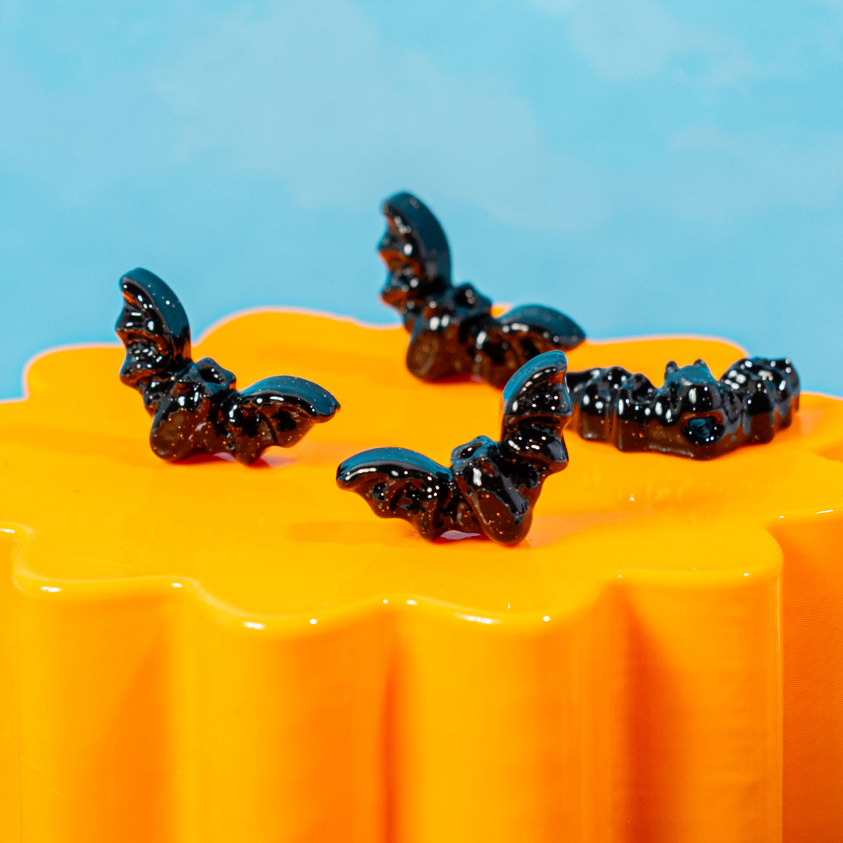 Four black bat kandi beads lined up on a wavy orange riser against a blue backdrop