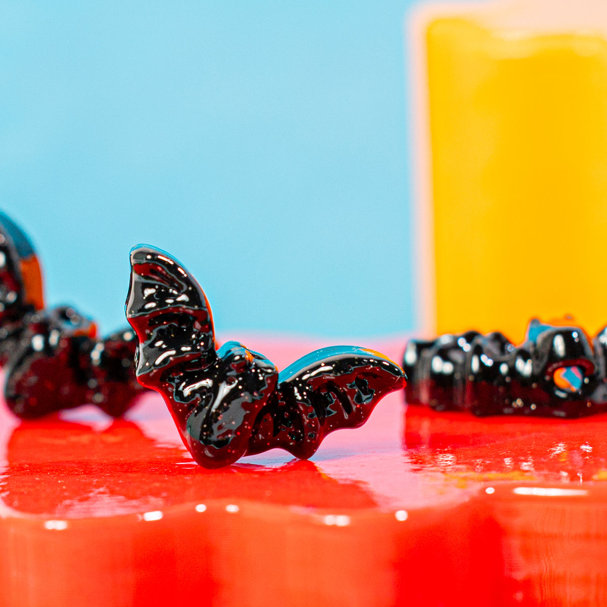 Black bat kandi bead on a glossy red riser with more bats blurred nearby
