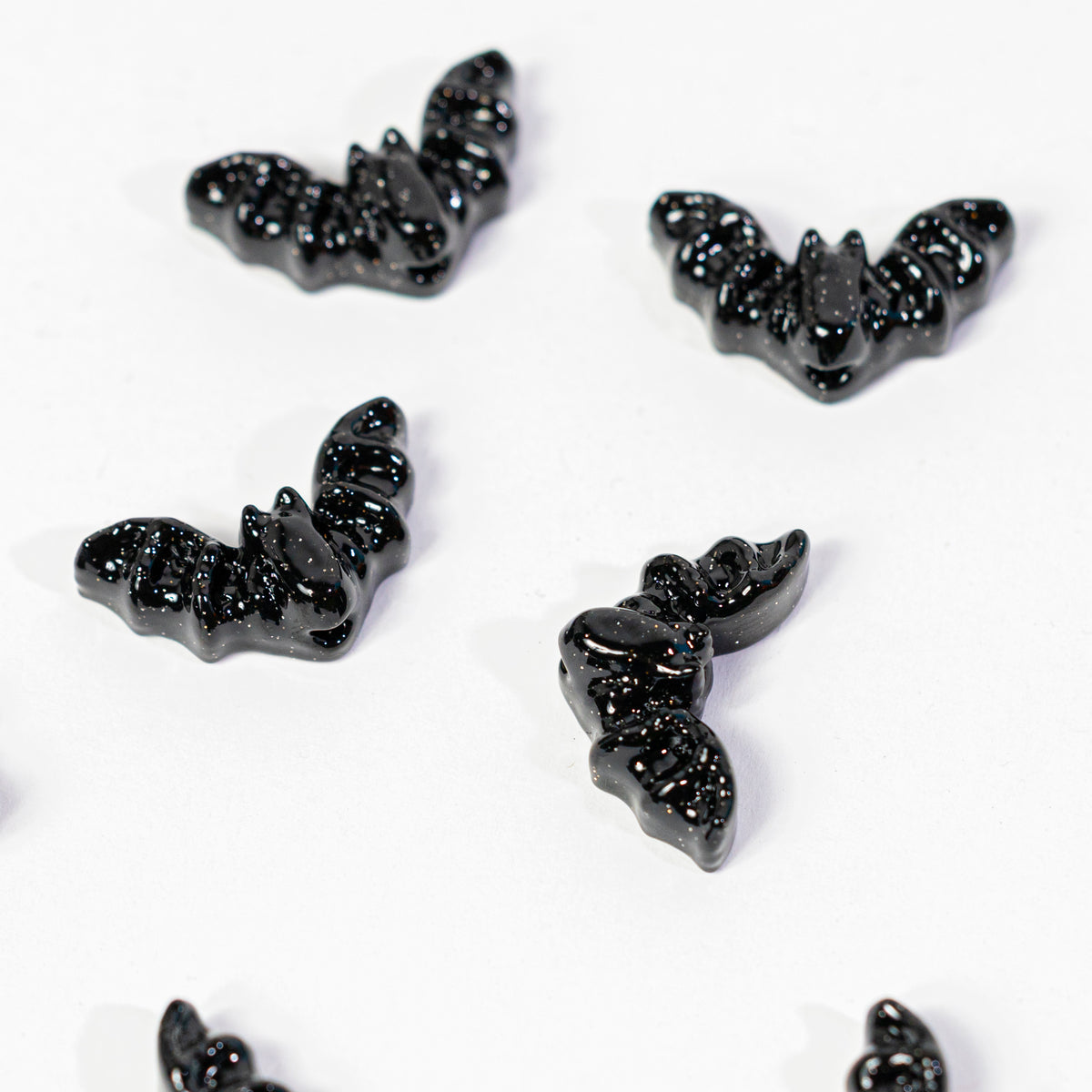 Close-up of five glossy black bat kandi beads on a white background