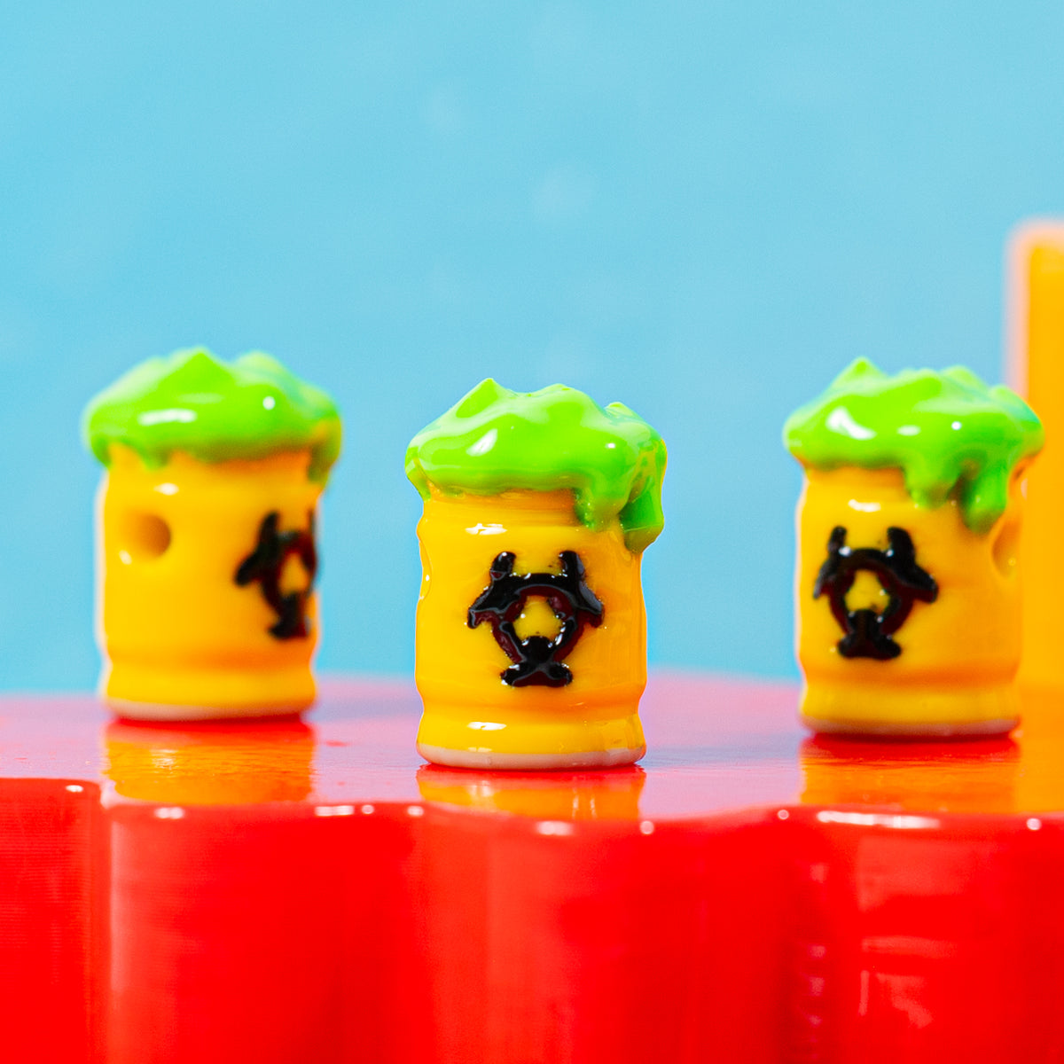Close-up of three yellow biohazard barrel kandi beads with green slime tops on a red riser