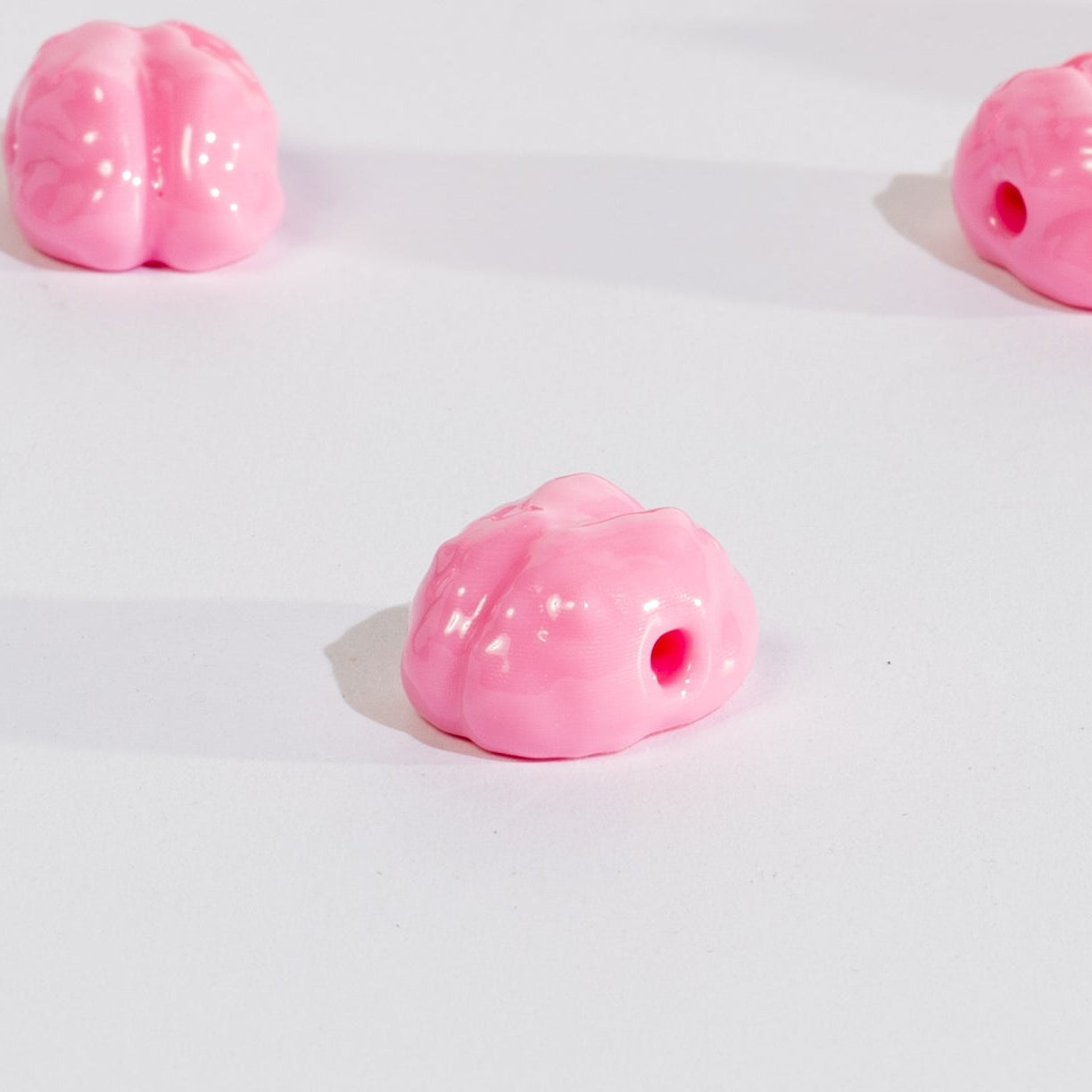 Close-up of one pink brain kandi bead on white, drilled hole visible, two more out of focus