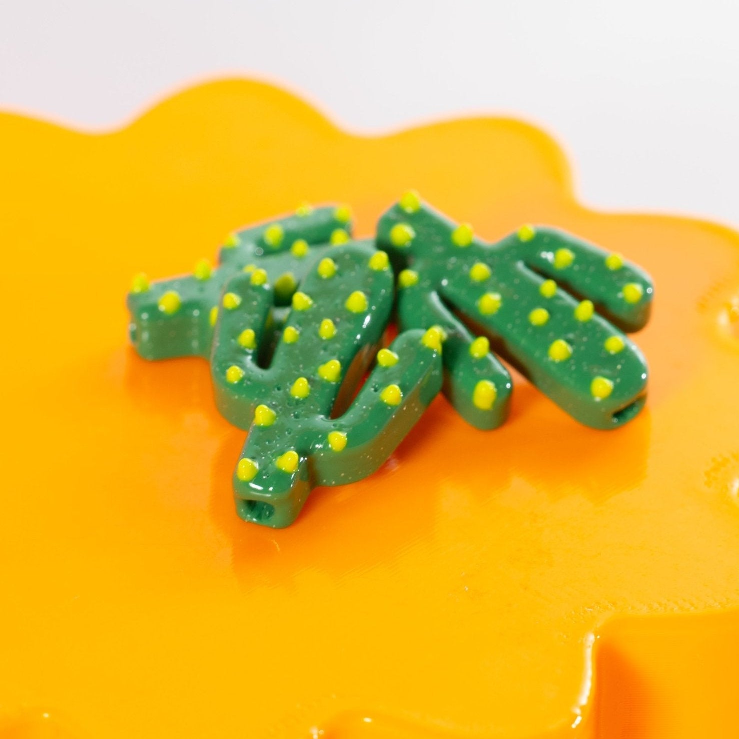 Two green cactus beads with yellow spines resting together on a glossy orange riser