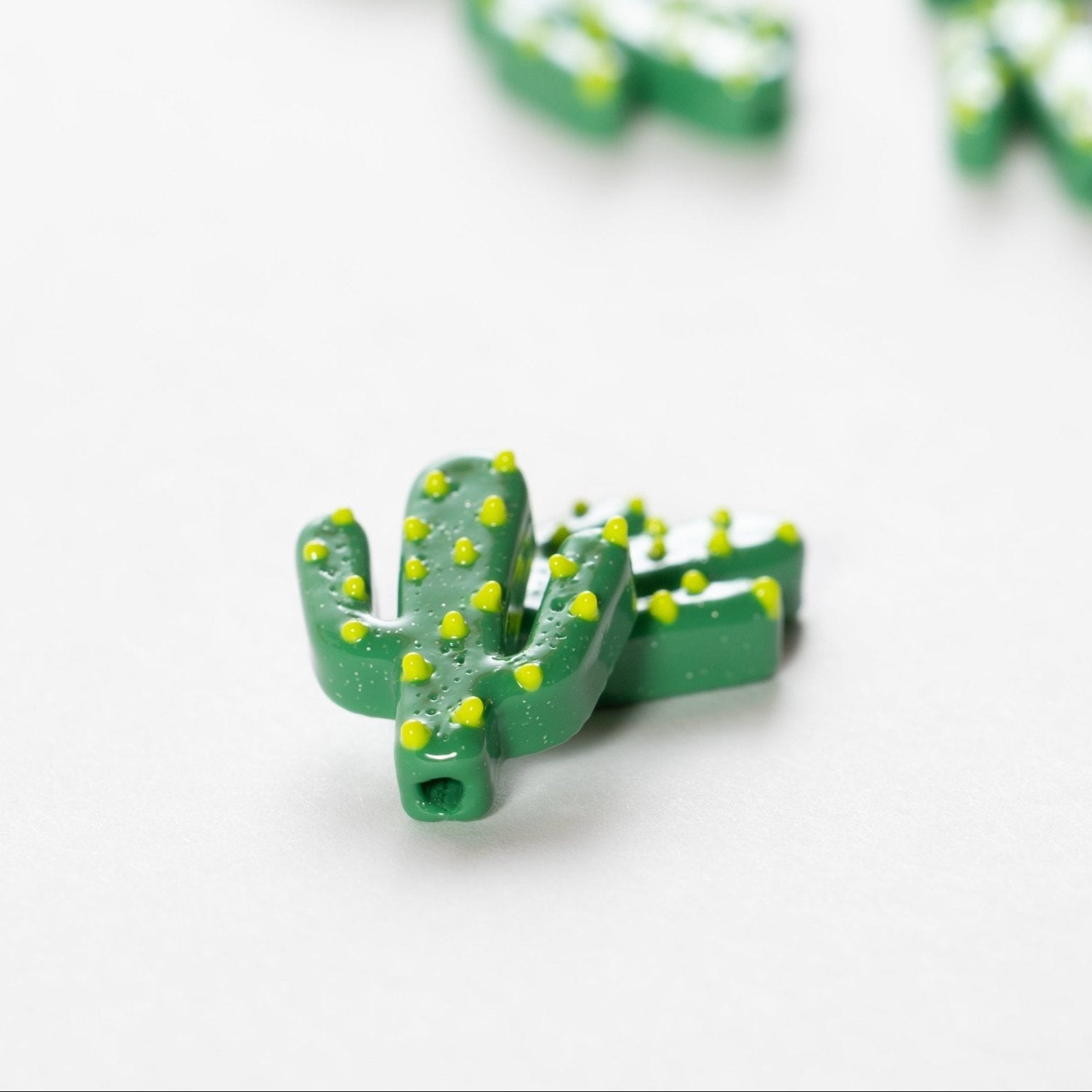 Close-up of a green cactus kandi bead with yellow spines, drilled hole visible at one end