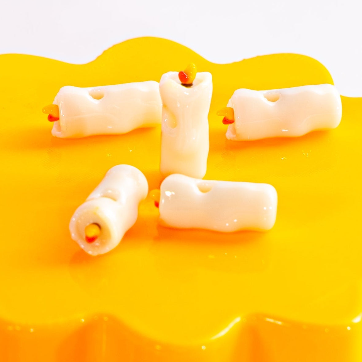 Five cream candle kandi beads on a yellow riser, one standing with its orange flame up