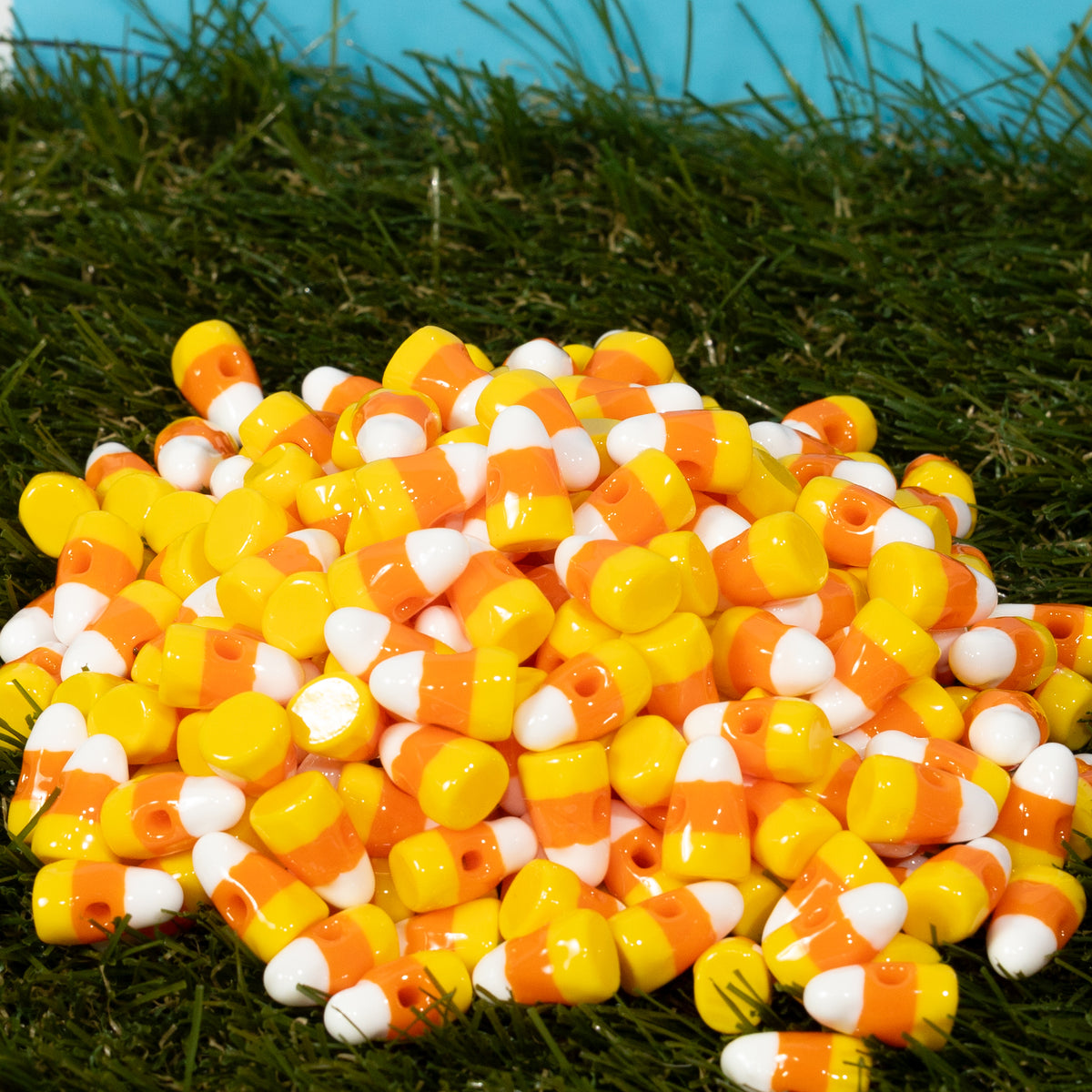 A heap of yellow, orange and white candy corn kandi beads on grass, drilled holes visible