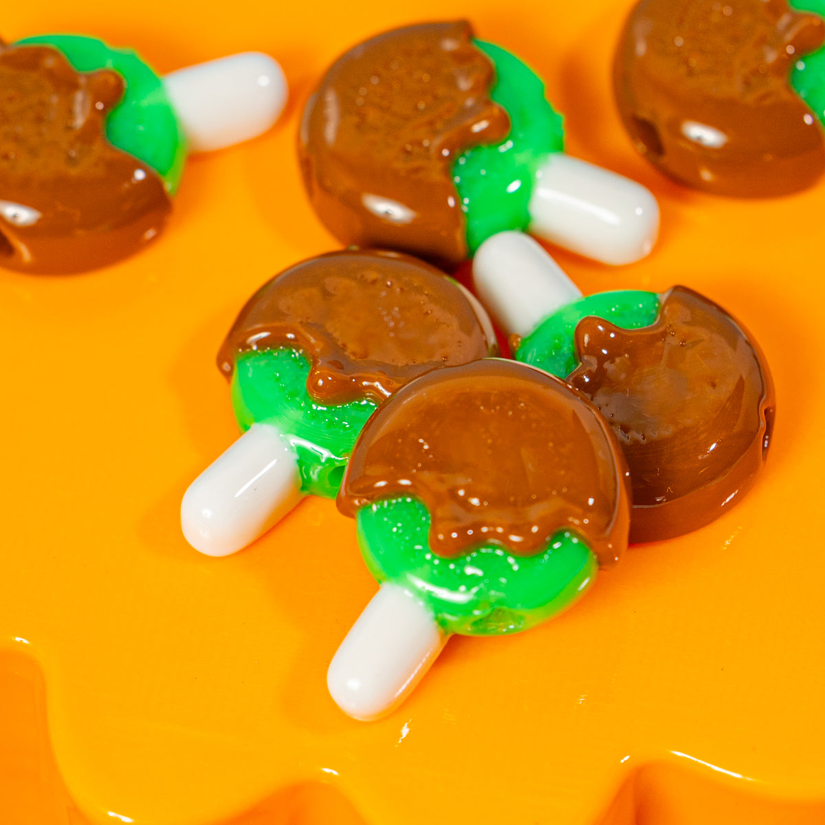 Close-up of caramel apple kandi beads with green apples and white sticks on an orange riser