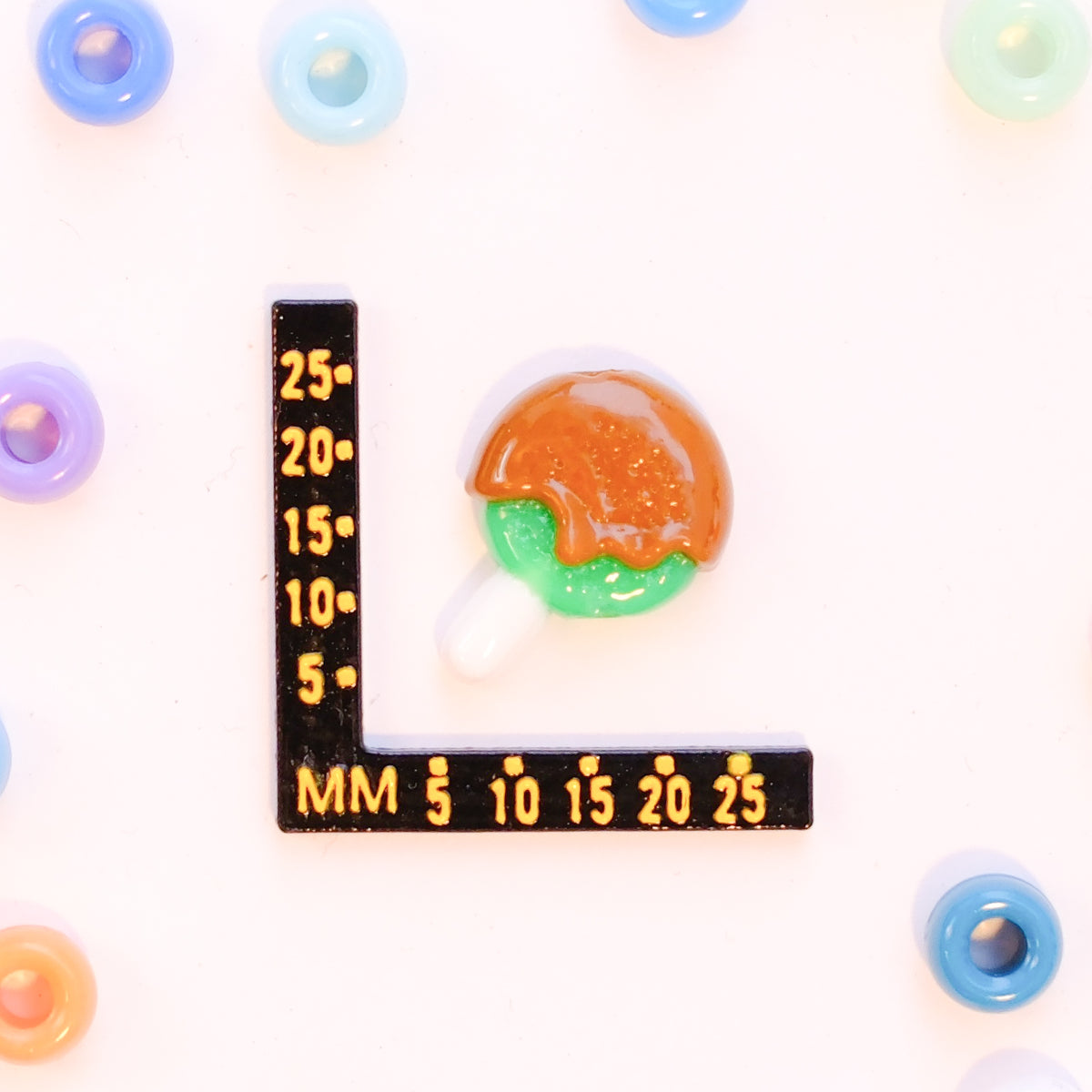 Size guide: a caramel apple kandi bead beside a millimeter ruler for scale