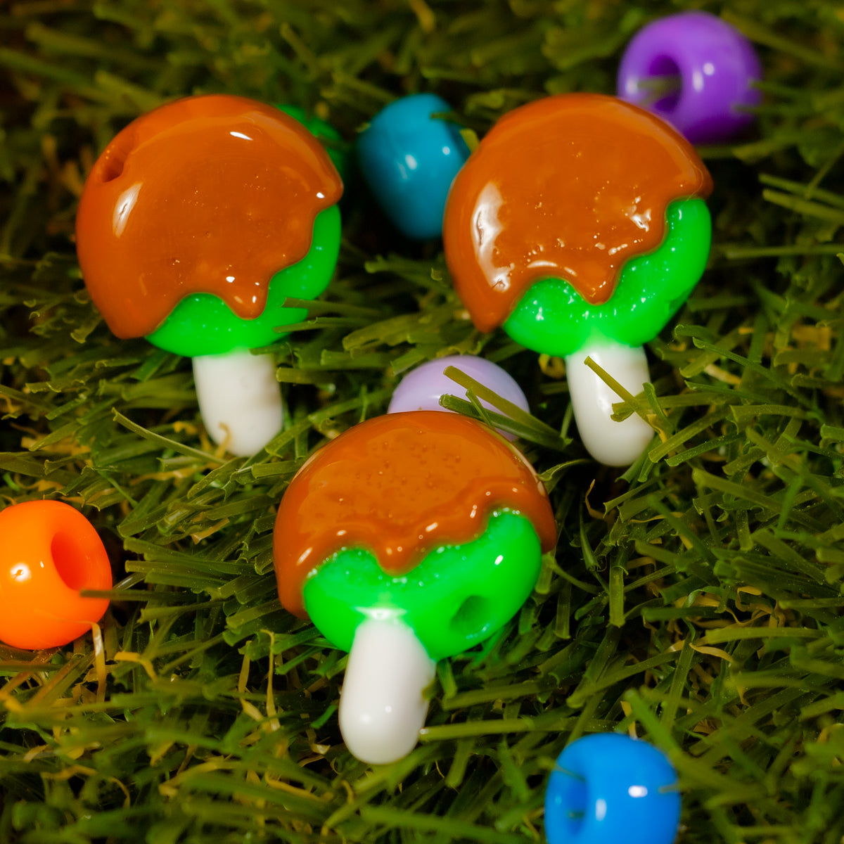 Three caramel apple kandi beads in green grass with colorful beads