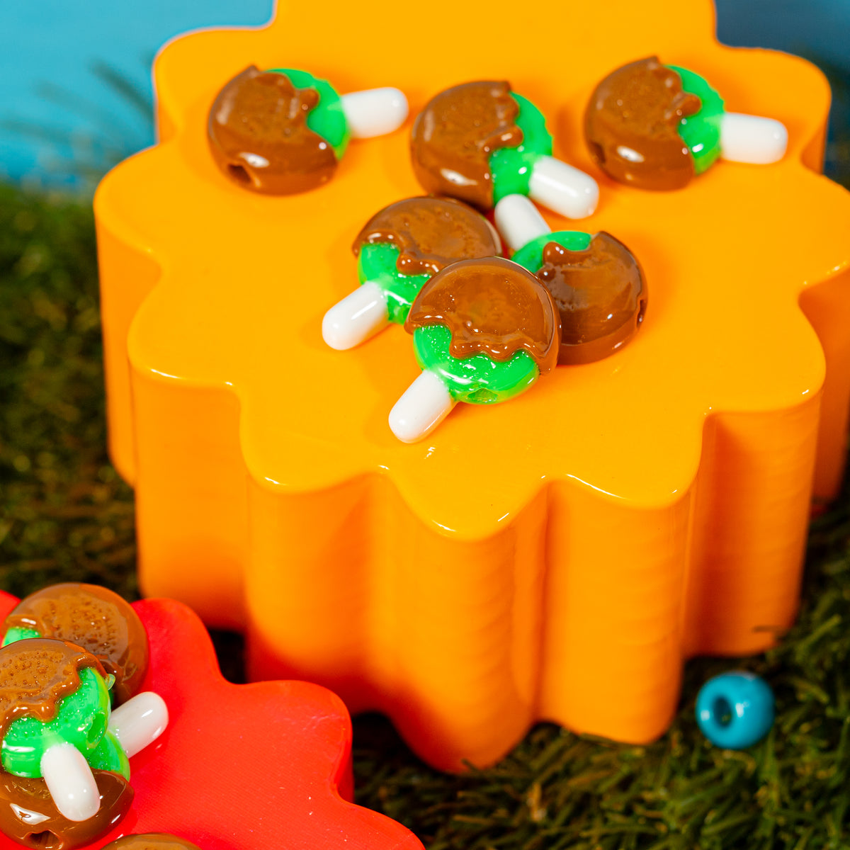 Caramel apple kandi beads on an orange riser surrounded by grass