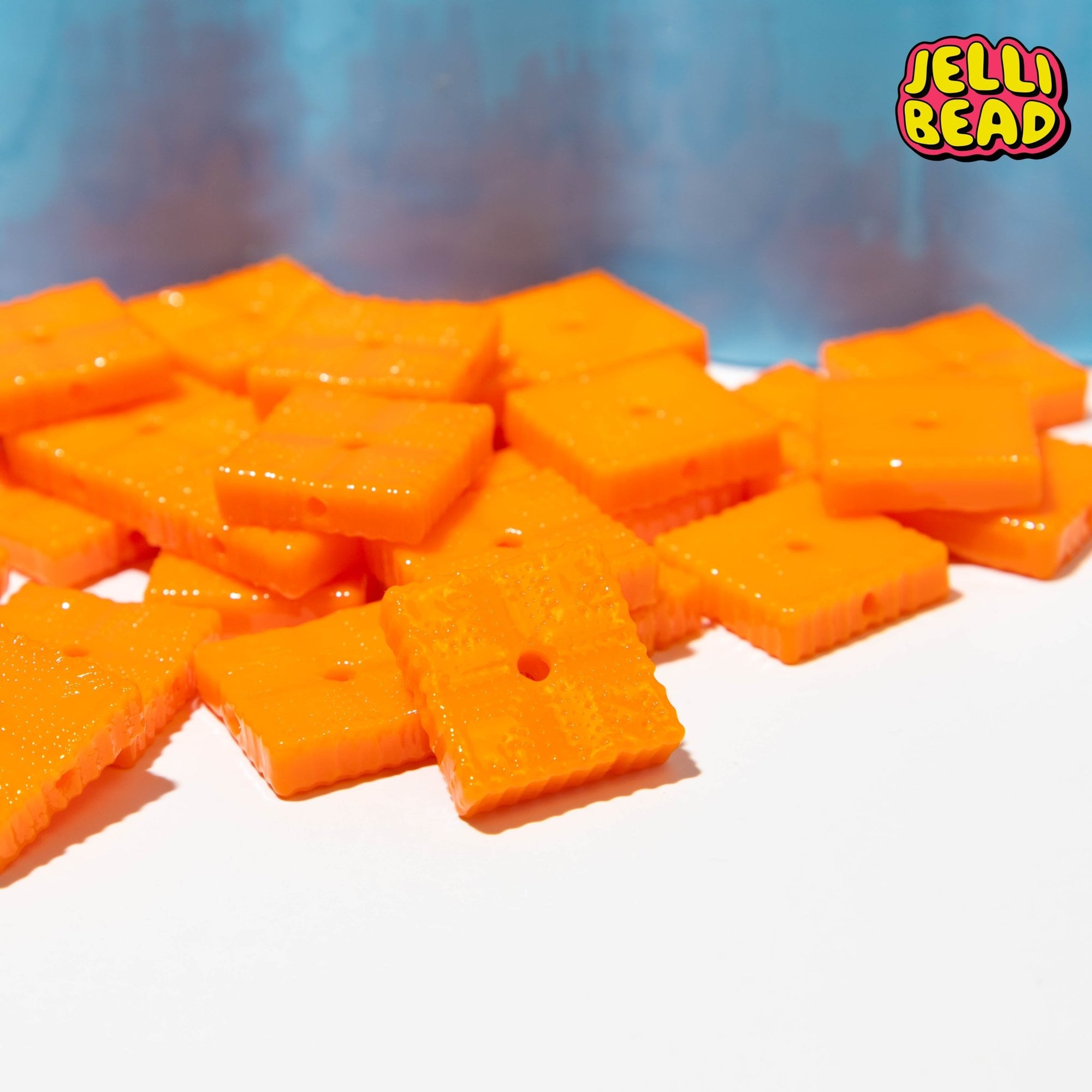 Orange cheese cracker beads for kandi bracelets heaped in a pile against a blue backdrop