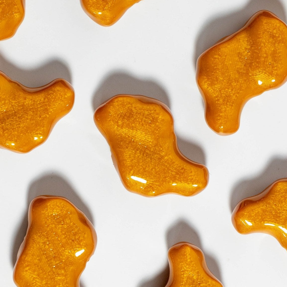 Glossy orange chicken nugget kandi beads spaced evenly on white, casting soft shadows from above