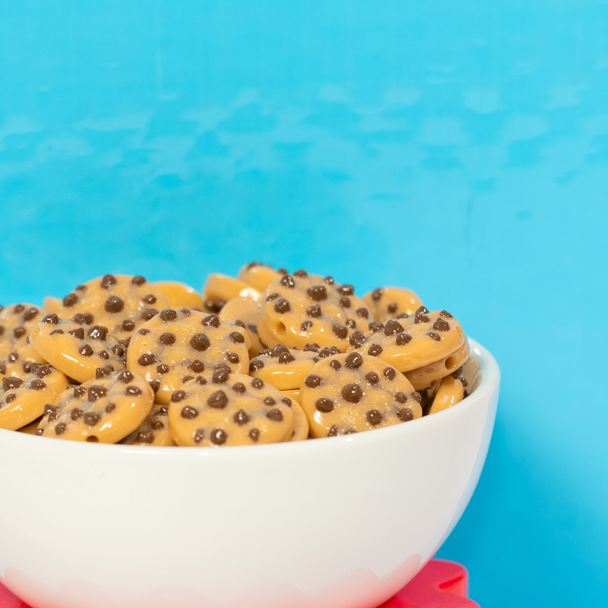 A white bowl heaped with chocolate chip cookie kandi beads against bright blue