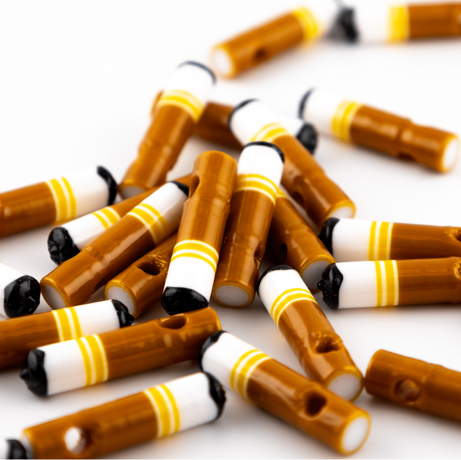Cigarette-shaped kandi beads with burnt black tips piled in a heap on white, drilled holes visible