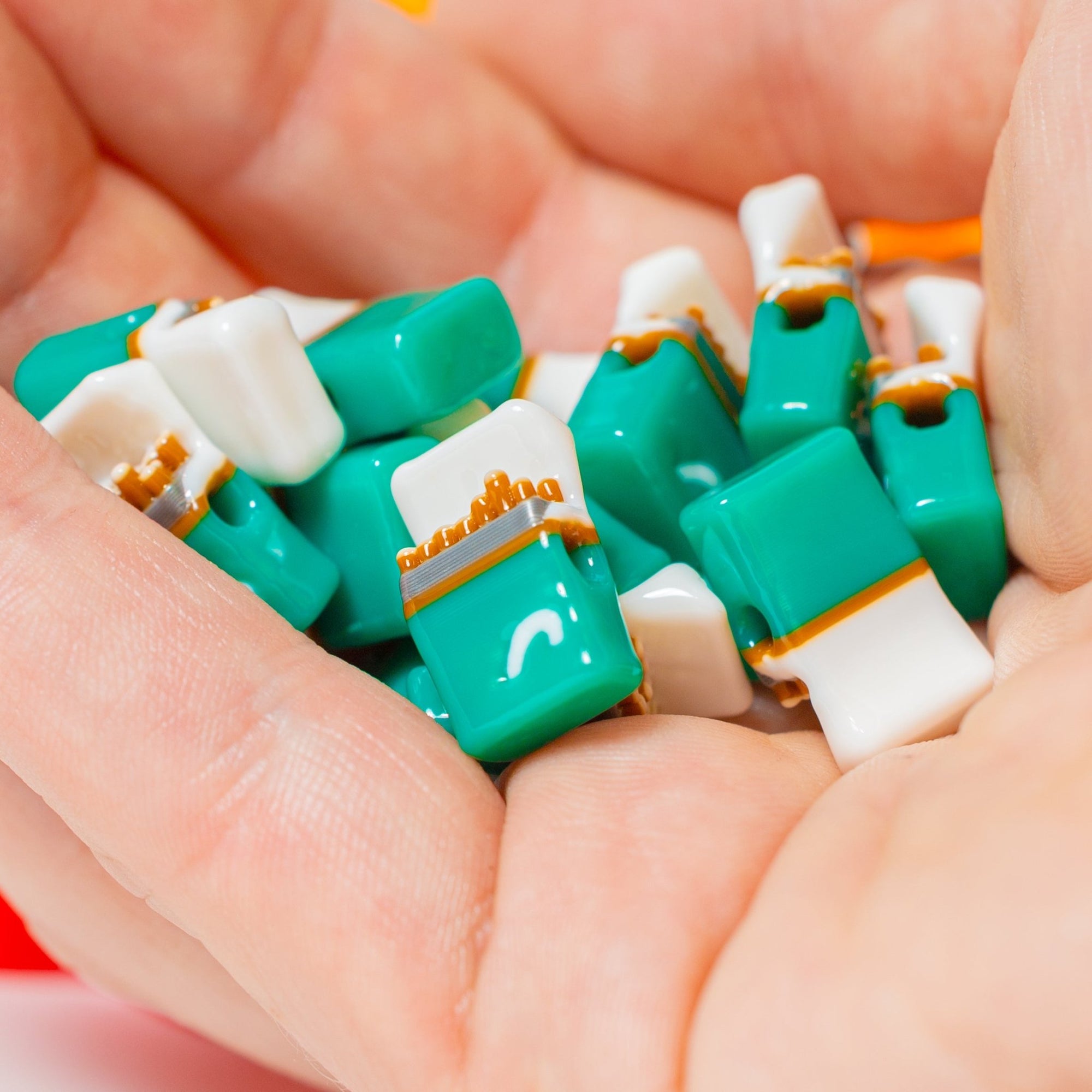 A palmful of teal and white cigarette-pack kandi beads held in a hand