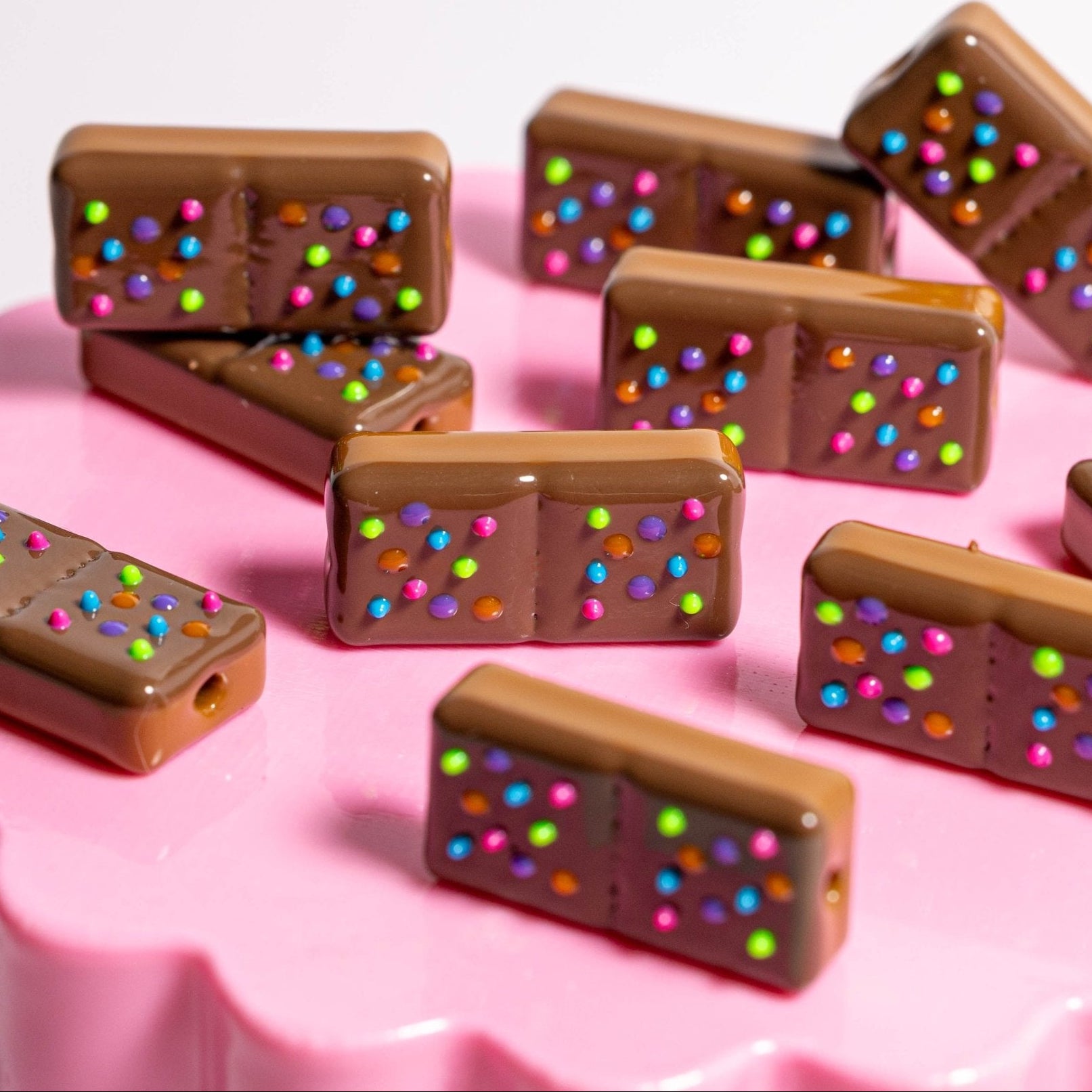 Chocolate brownie kandi beads with candy-dot sprinkles tilted across a pink fluted cake stand