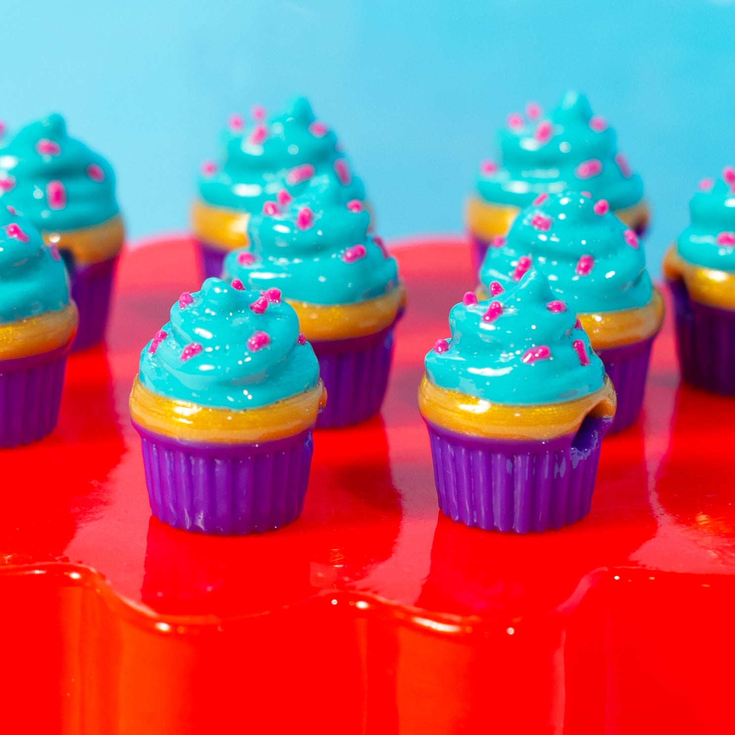 Turquoise-frosted cupcake kandi beads with purple wrappers and pink sprinkles on a red riser