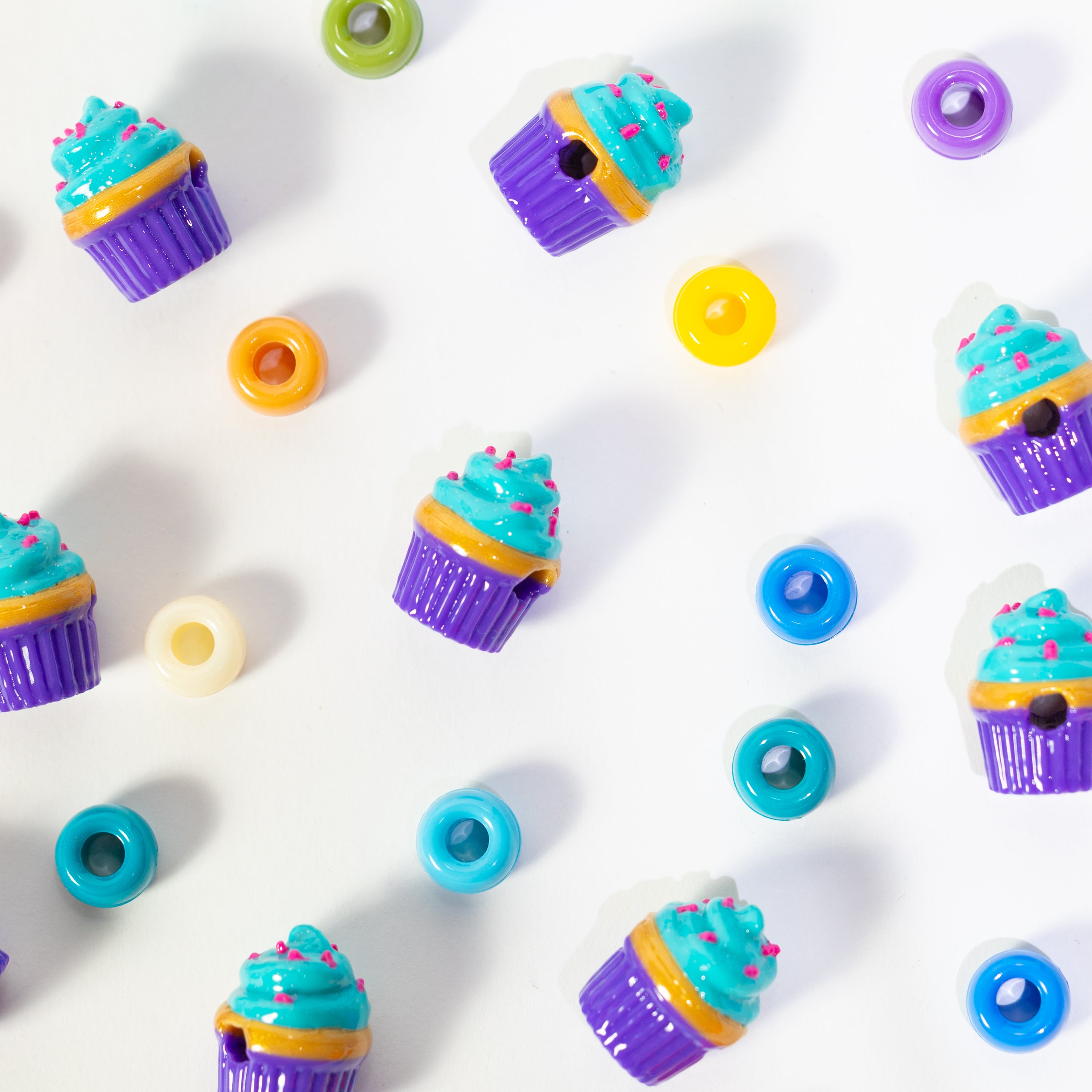 Cupcake kandi beads scattered on white among rainbow pony beads, drilled holes visible