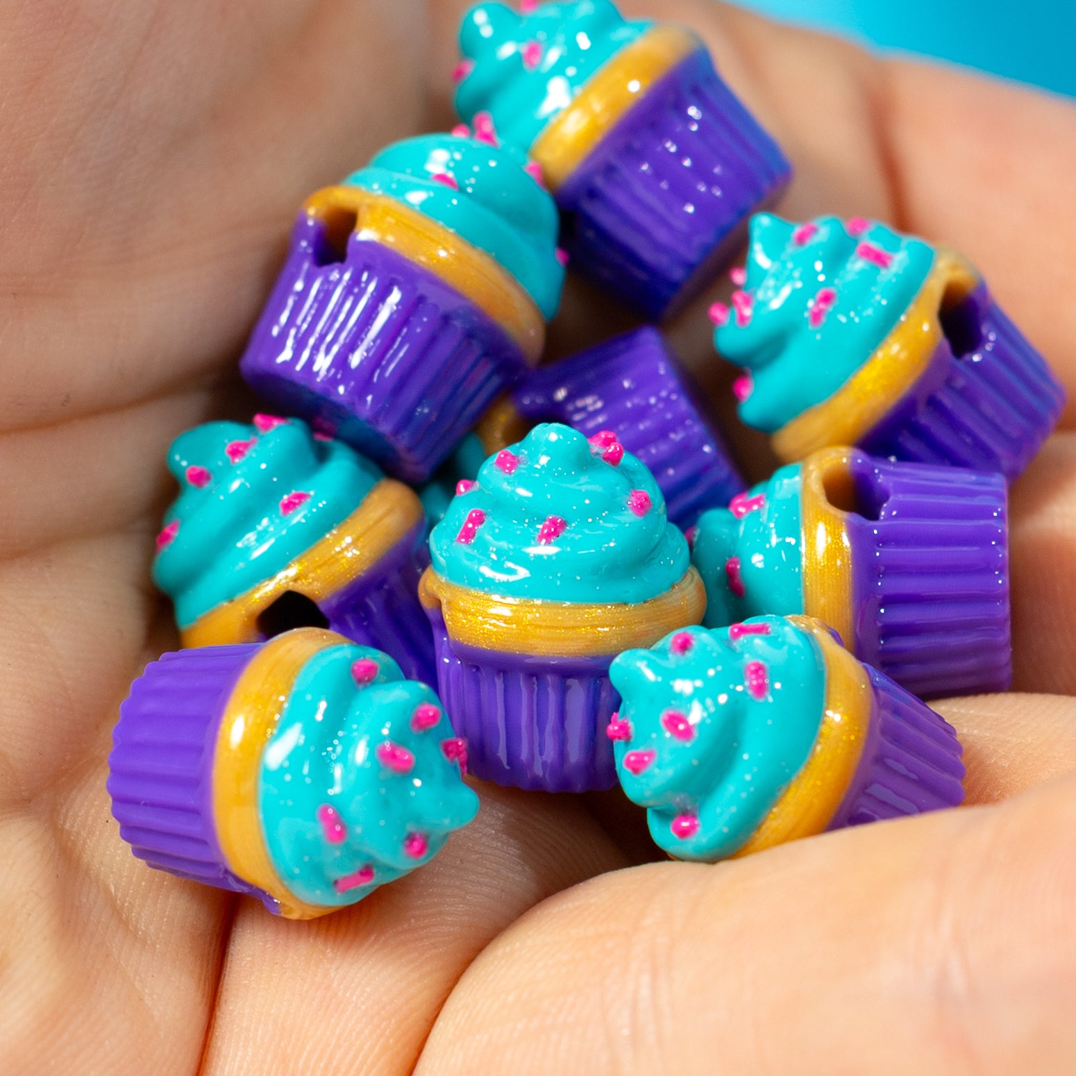 A palmful of turquoise and purple cupcake kandi beads topped with hot pink sprinkles