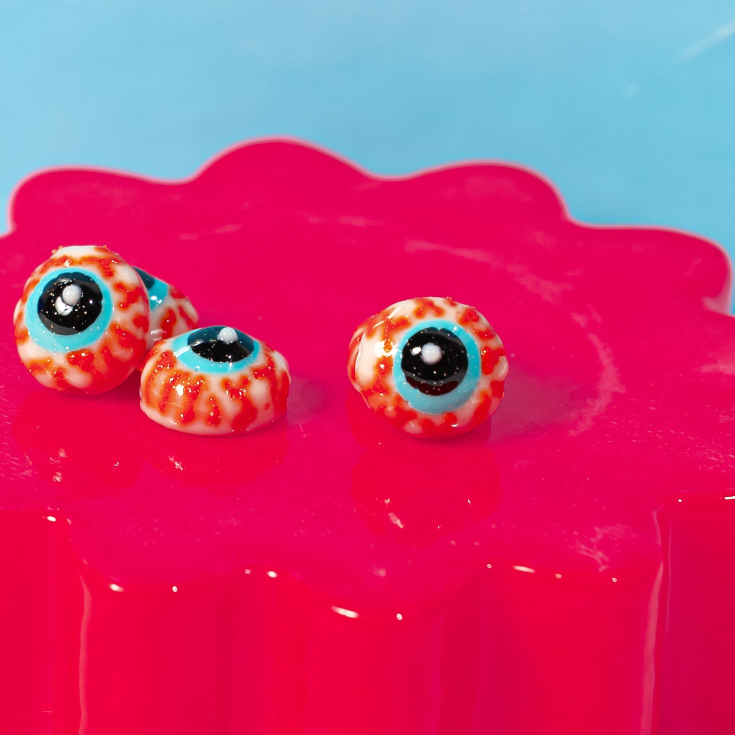 Close-up of three bloodshot eyeball kandi beads with turquoise irises on a hot pink riser