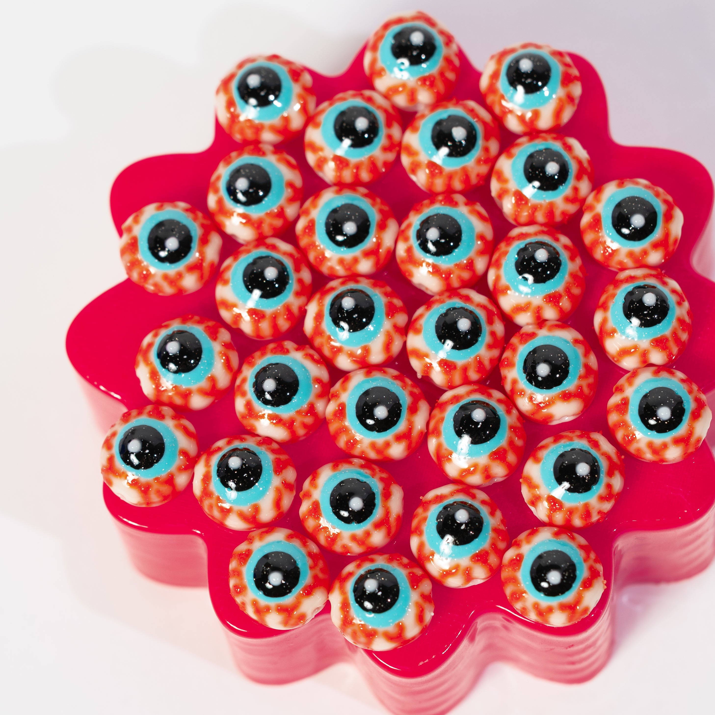 Two dozen red-veined eyeball kandi beads packed across a hot pink riser