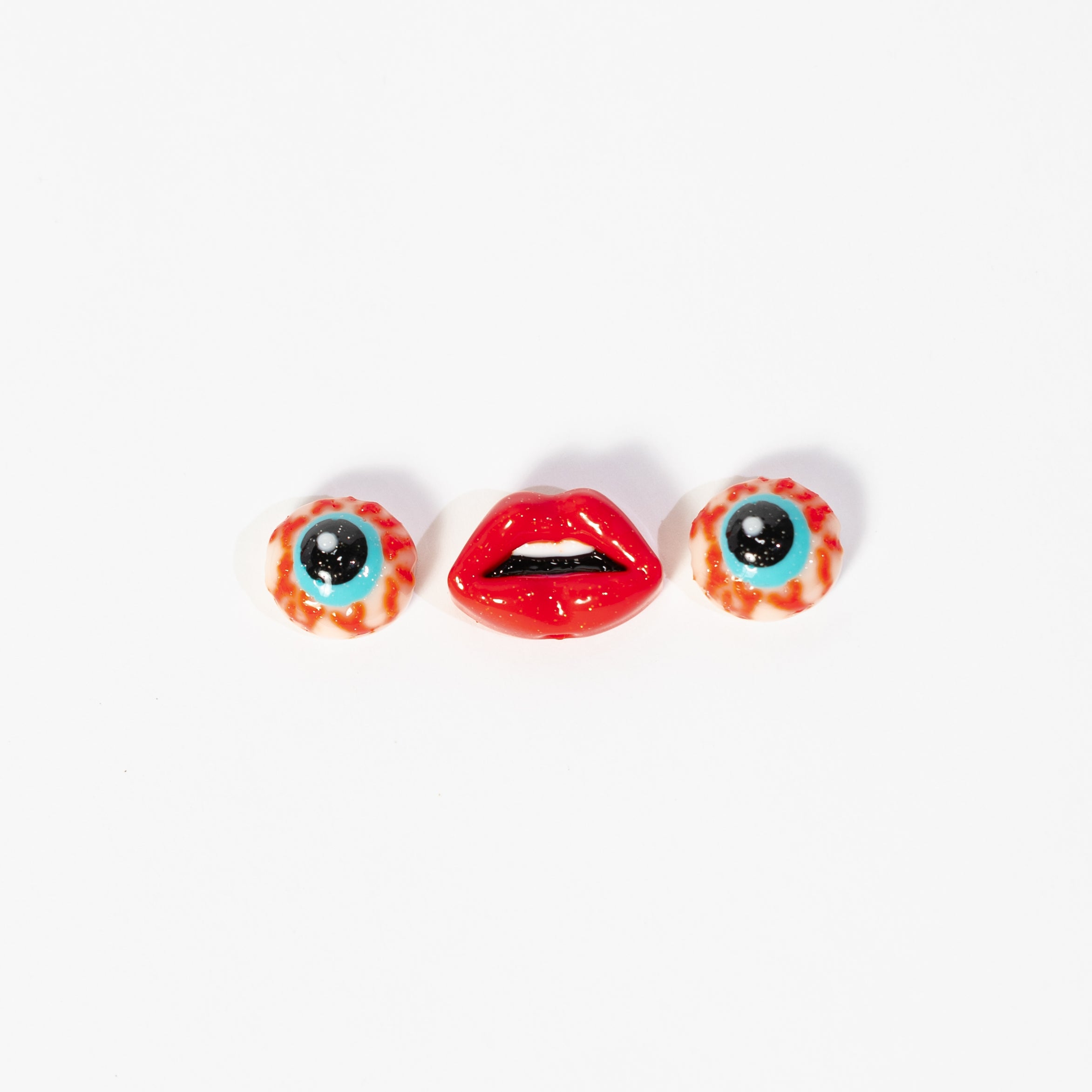 Two eyeball kandi beads either side of a glossy red lips bead on white