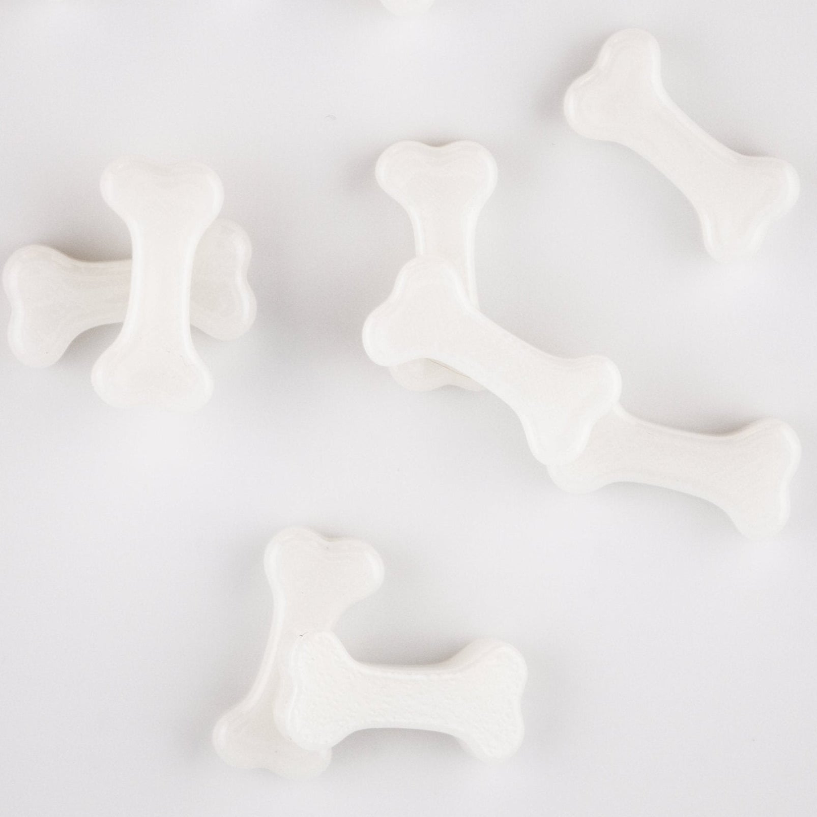 White bone kandi beads spread apart on a pale surface, from above