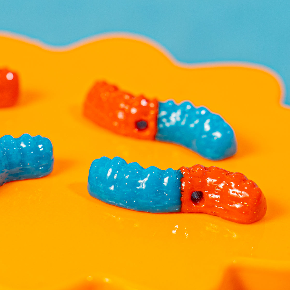 Close-up of orange and blue gummy worm kandi beads on an orange riser, drilled holes visible