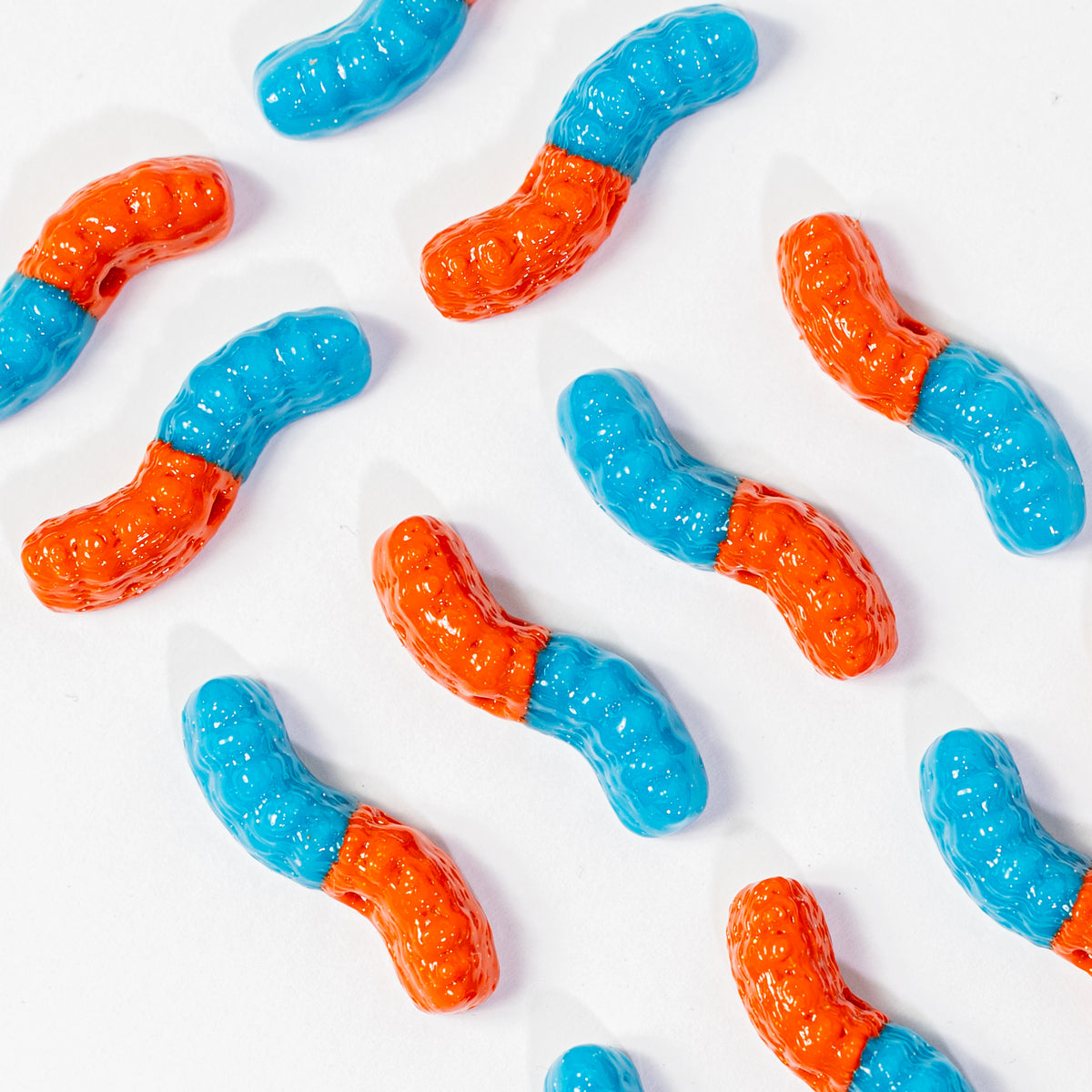 Orange and blue gummy worm kandi beads scattered on white