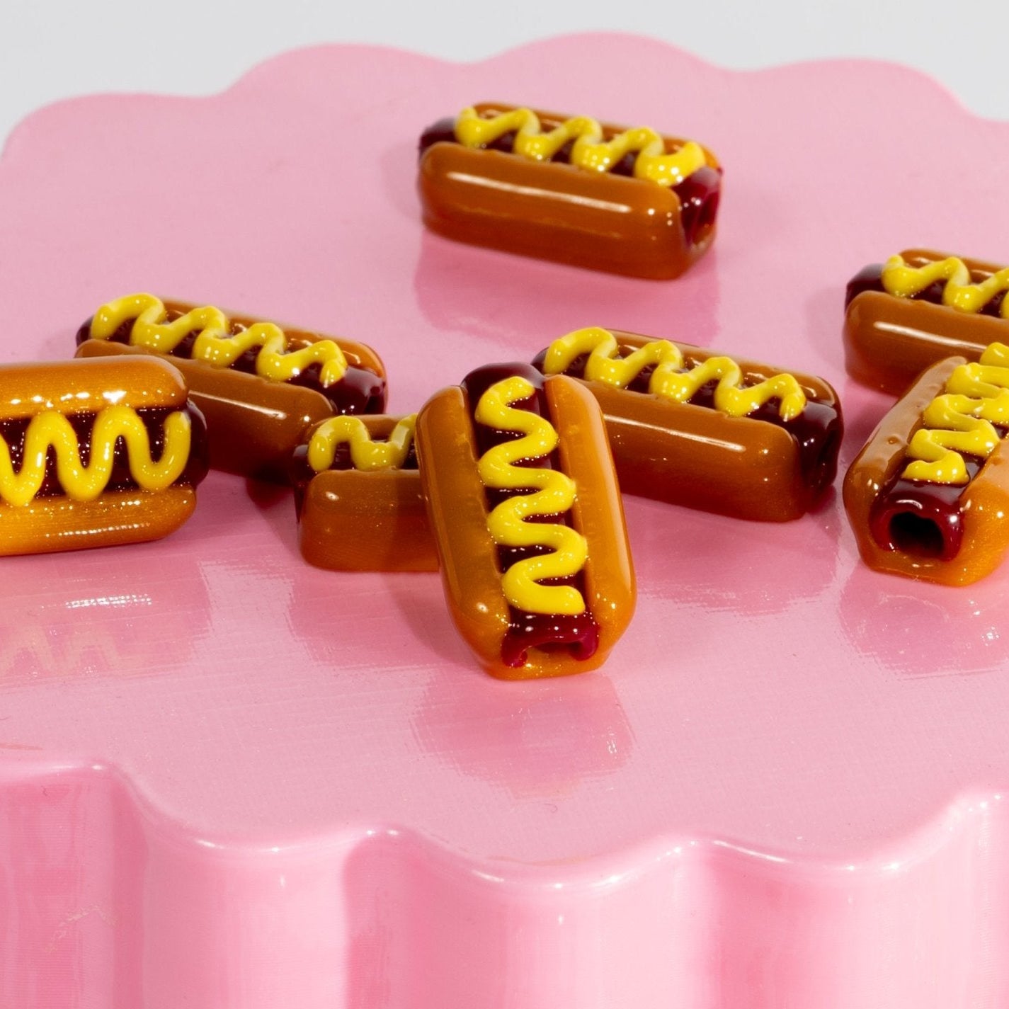 Hot dog kandi beads with mustard zigzags scattered on a pink scalloped plate, one hole facing out