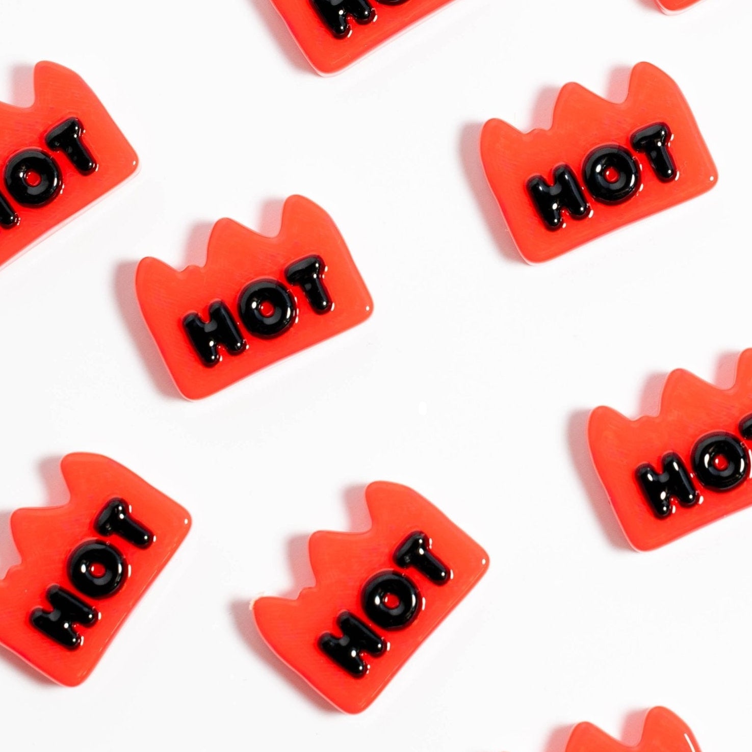 Red flame-shaped kandi beads reading HOT in black, scattered in diagonal rows on white
