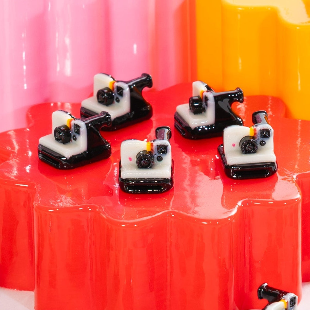 Five white and black instant camera kandi beads lined up across a glossy red riser