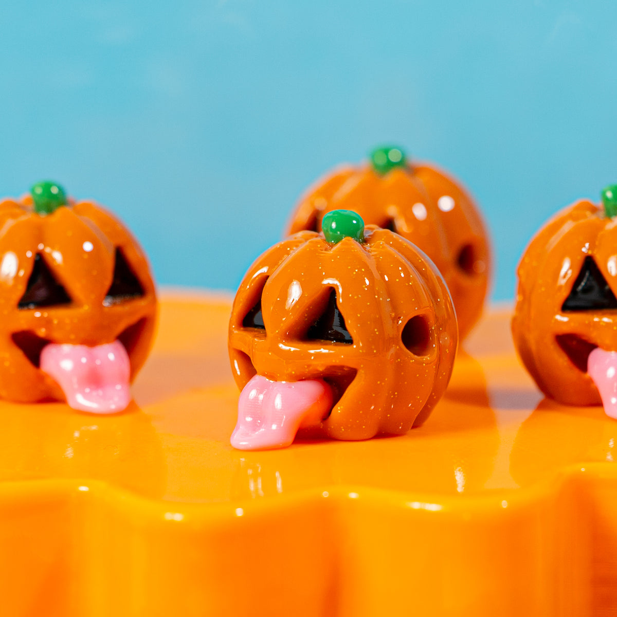 Close-up of orange jack o lantern kandi beads with pink tongues and green stems on an orange riser