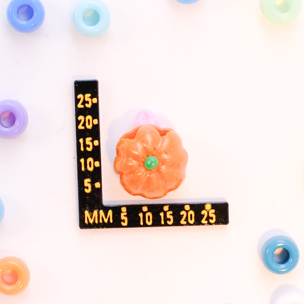Size guide: a jack o lantern kandi bead beside a millimeter ruler for scale
