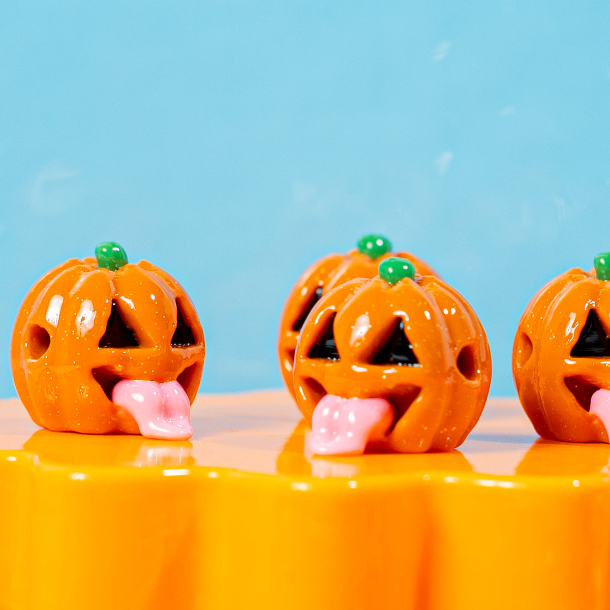 Row of grinning jack o lantern kandi beads sticking out pink tongues on an orange riser