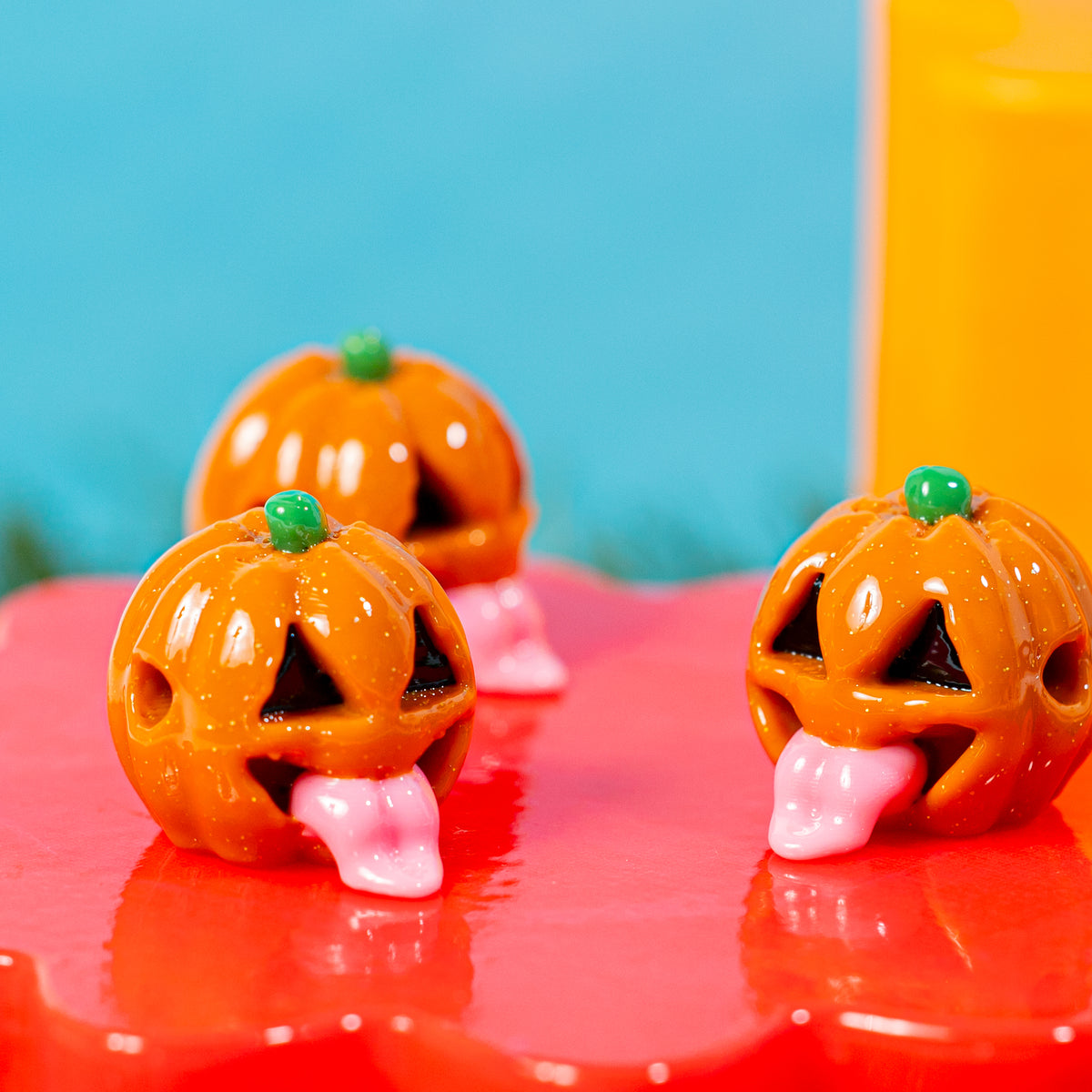 Three orange jack o lantern kandi beads on a glossy red riser
