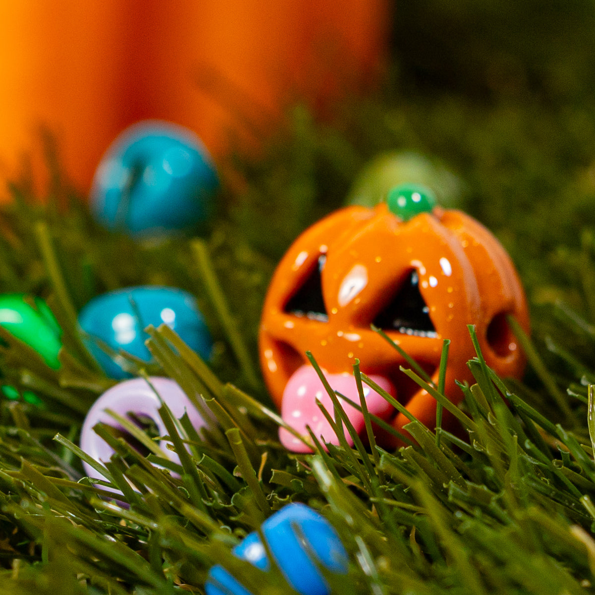 Jack o lantern kandi bead with a pink tongue in green grass beside colorful beads