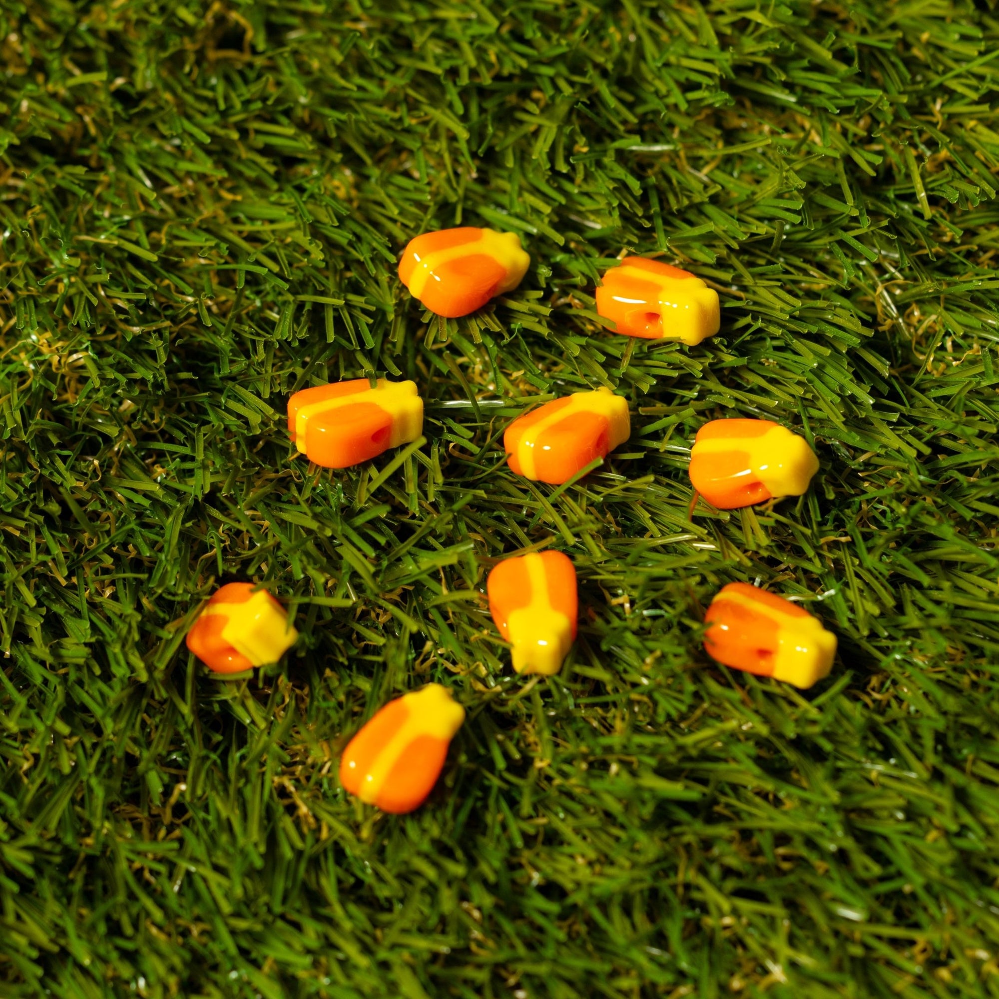 Candy corn kandi beads in orange and yellow, scattered across artificial grass