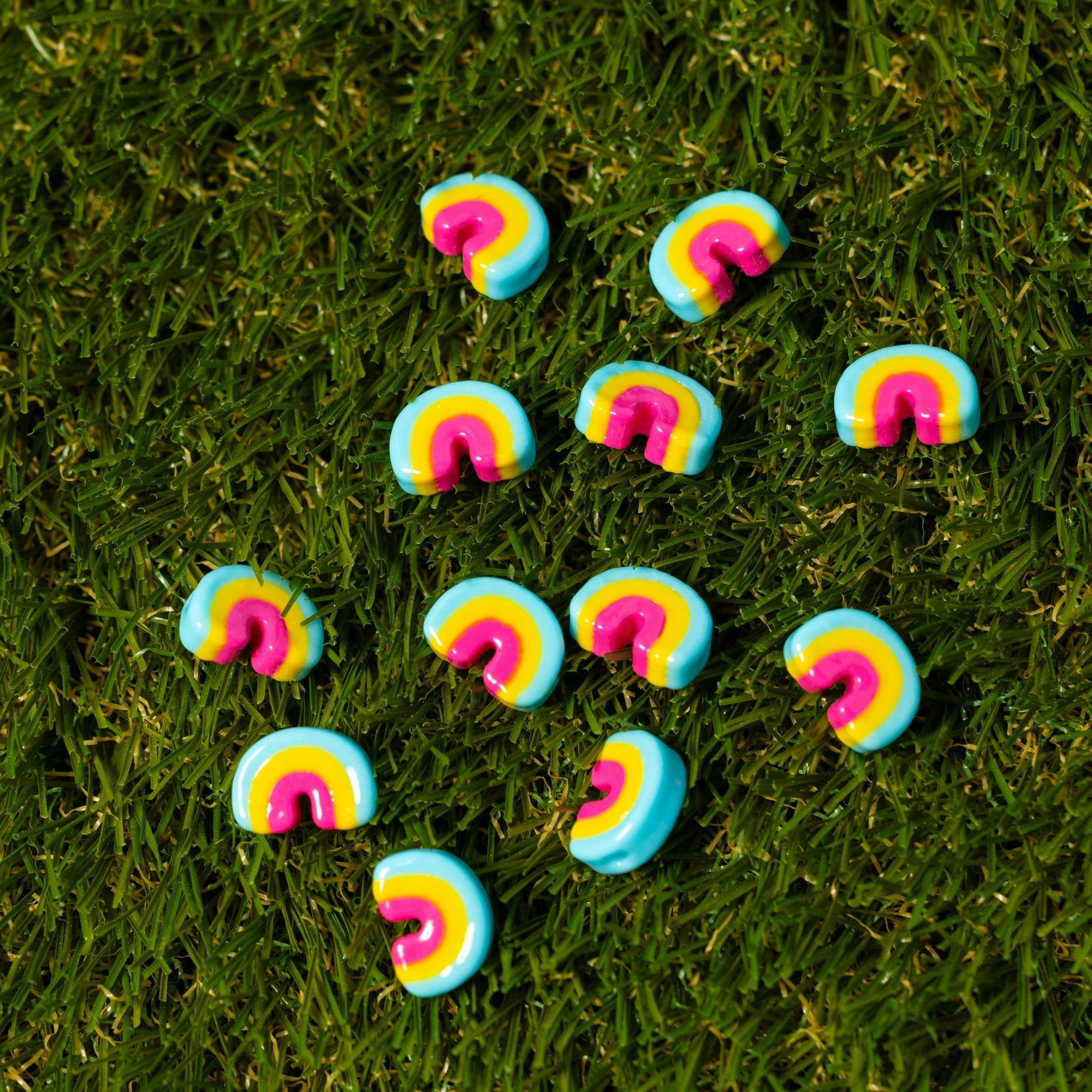 Rainbow arch kandi charms in pink, yellow and blue scattered on artificial grass