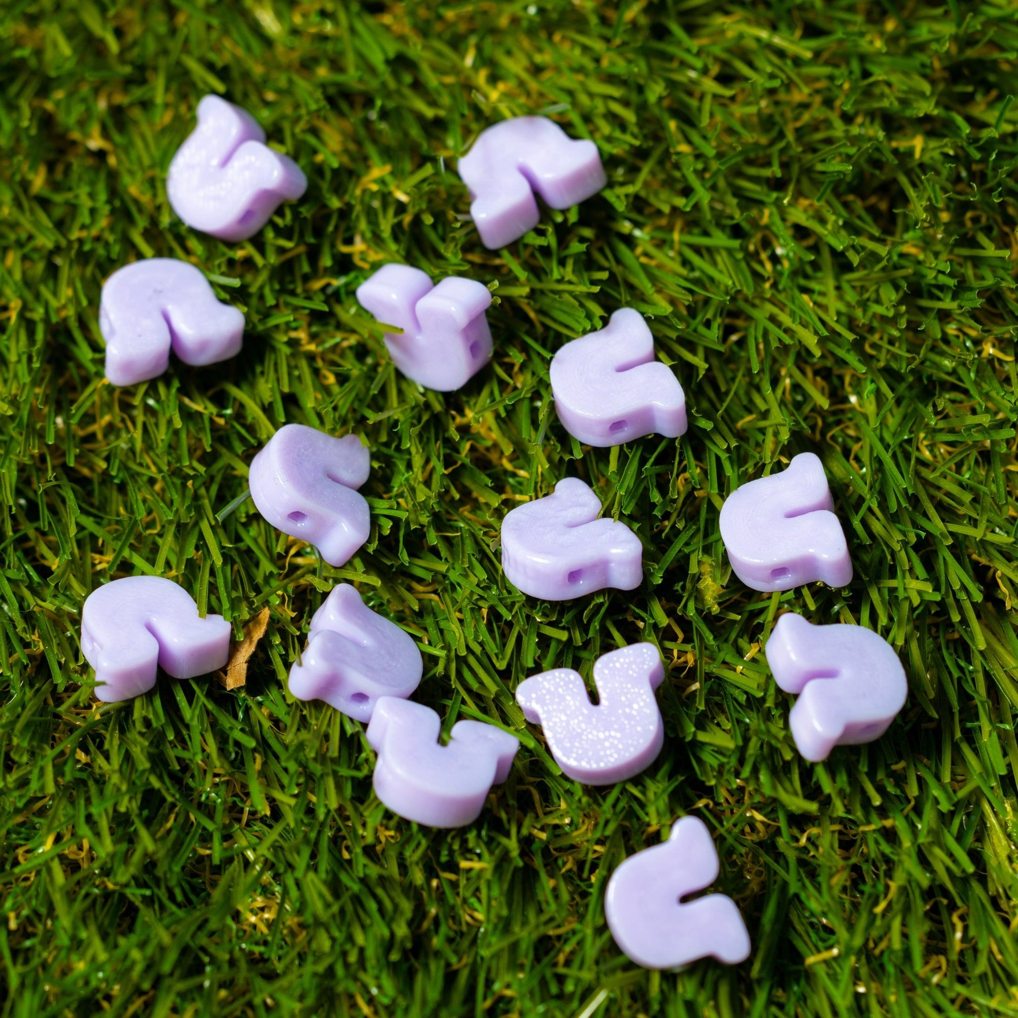 Lavender horseshoe-shaped kandi charms scattered on turf, holes visible on several